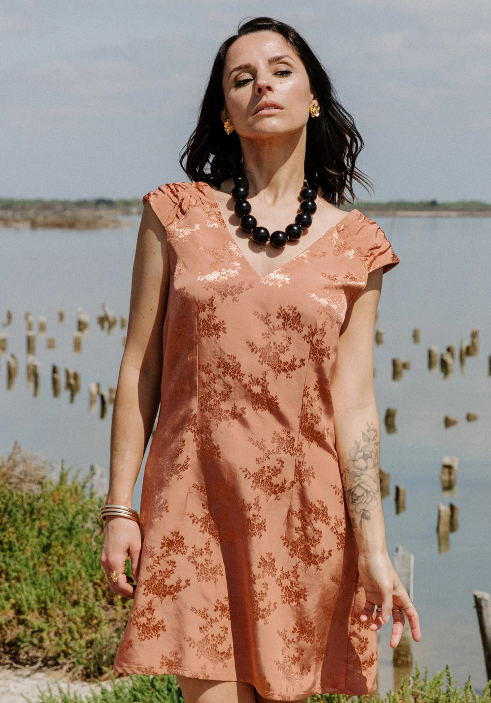Woman wearing the Pétula Dress sewing pattern from Maison Fauve on The Fold Line. A sleeveless dress pattern made in viscose crepe or poplin, fine jacquard, or lace fabric, featuring an A-line silhouette shaped with darts, V-neckline, and gathered shoulder panels.