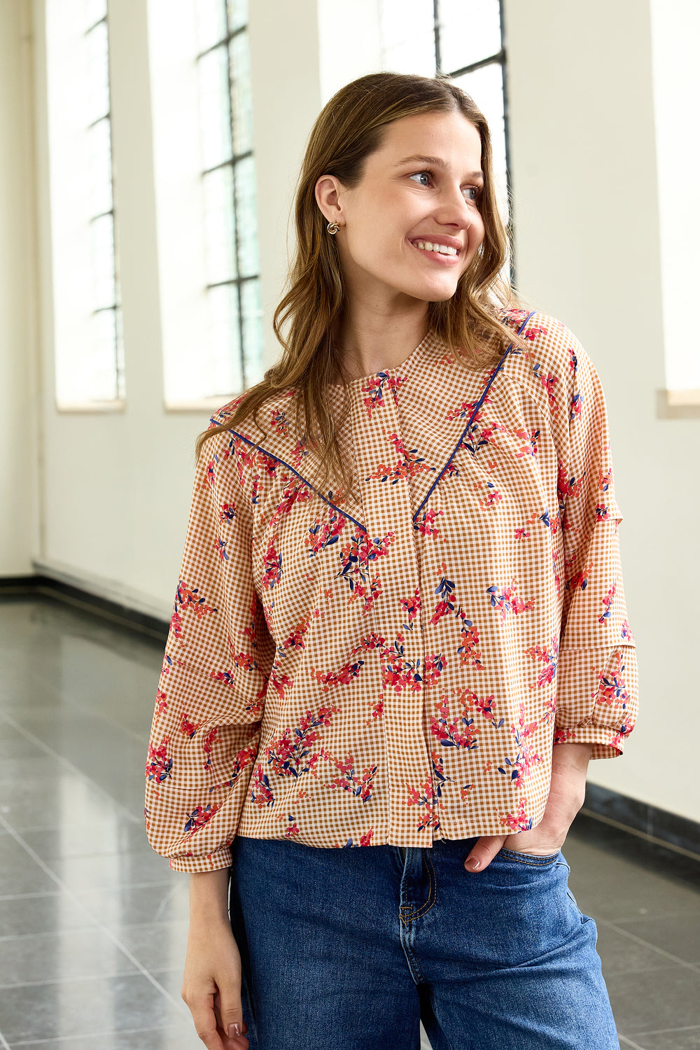 Woman wearing the Phoebe Blouse sewing pattern from Atelier Jupe on The Fold Line. A top pattern made in cotton, viscose, linen, tencel, or polyester fabric, featuring a round neckline, V-shaped front yoke with piping, hidden button placket, and 3/4 sleeves with horizontal pleats and cuffs.
