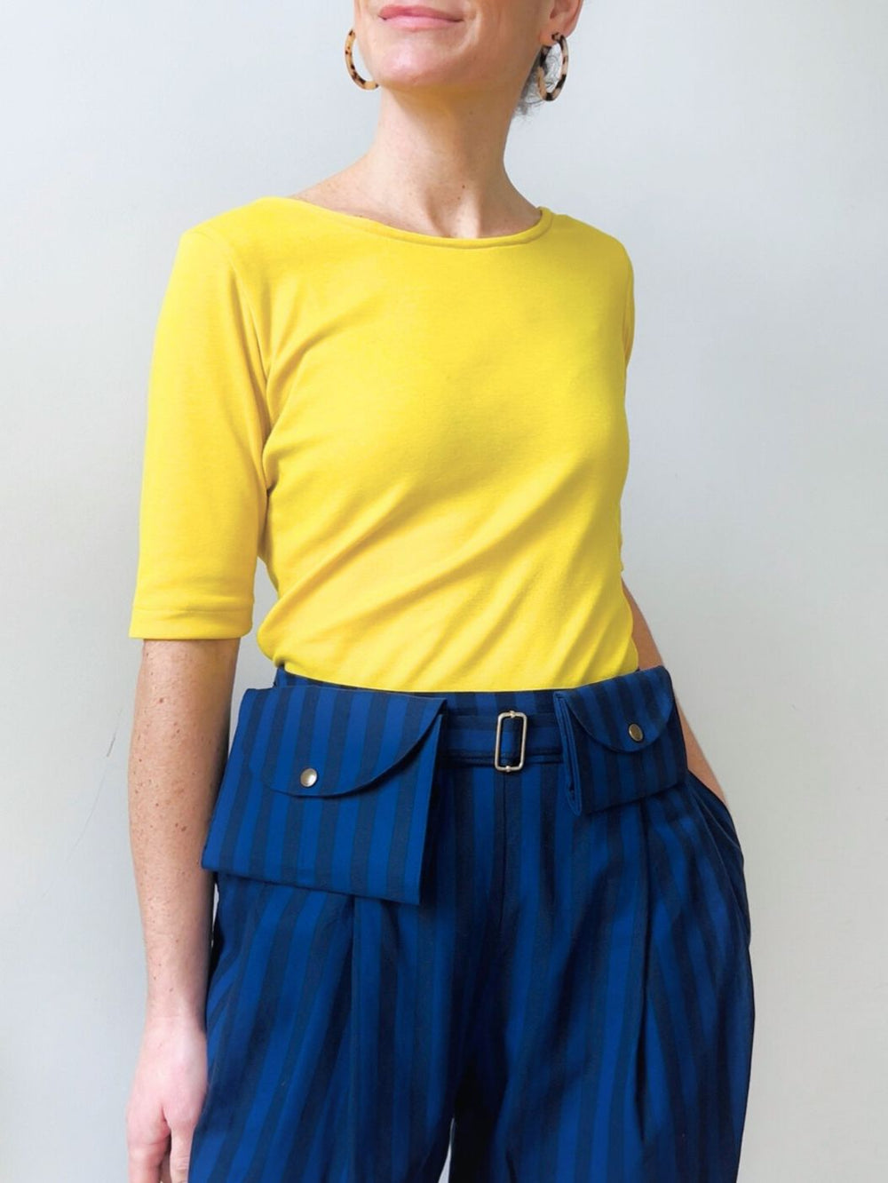 Woman wearing the Pip Pouch sewing pattern from Notches on The Fold Line. A belt bag pattern made in cotton fabric, featuring two sizes and a snap closure.