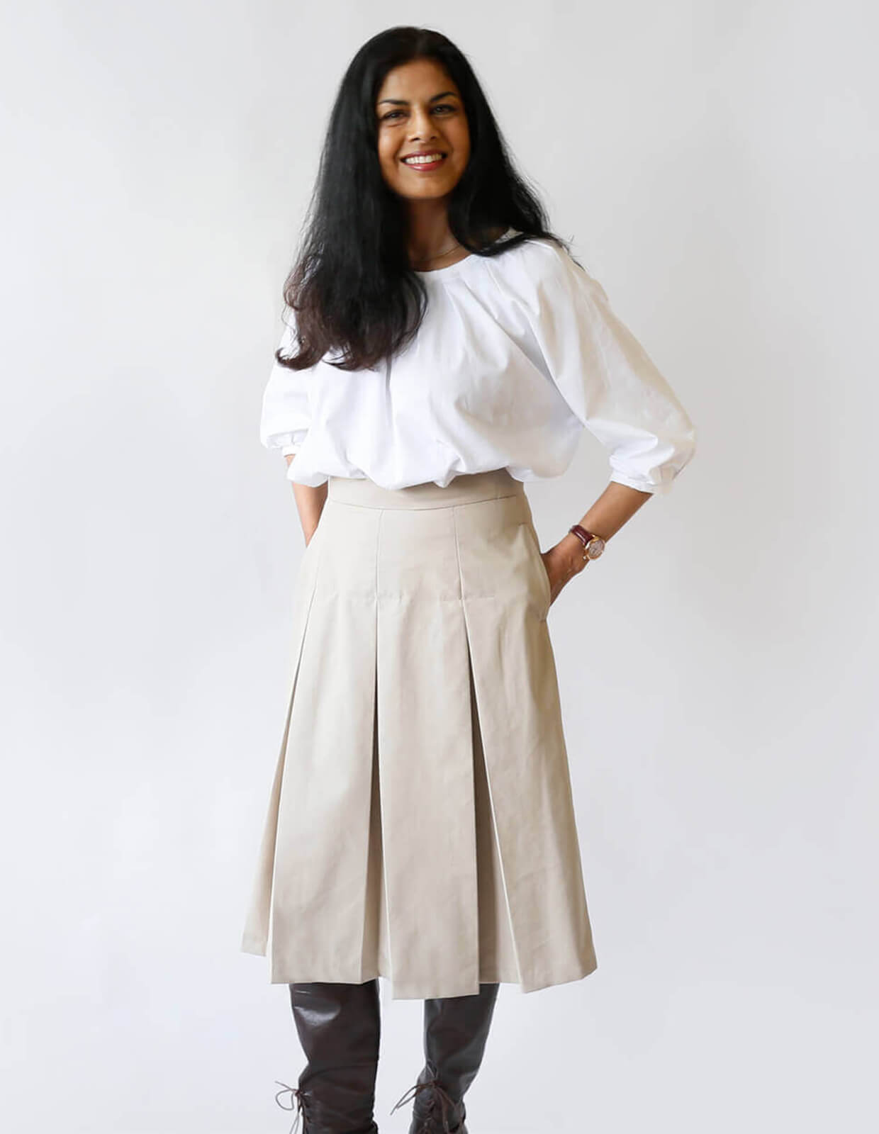 Woman wearing the Pleated Skirt sewing pattern from The Maker's Atelier on The Fold Line. A knee length skirt pattern made in cotton, linen, wool, or crepe fabric, featuring box pleats and side seam pockets.