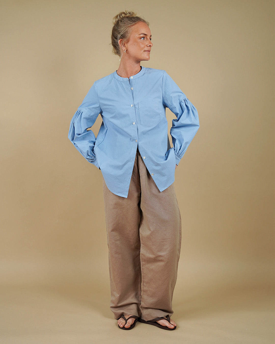 Woman wearing the Puff Shirt sewing pattern from Wardrobe by Me on The Fold Line. A shirt pattern made in cotton or linen fabric, featuring a round neckline, button front, long sleeves with voluminous gathers, and a curved hem.