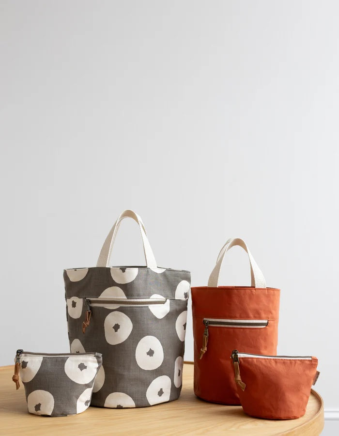The Quarry Tote sewing pattern from Noodlehead on The Fold Line. A bag pattern made in mid-weight canvas, dry oilskin, waxed canvas/twill, or vinyl fabric, featuring two sizes with a flat base, handles, zippered front pocket, and interior mesh slip pocket, and a bonus zippered pouch.
