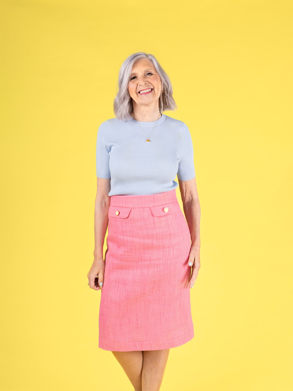 Woman wearing the Ramona Skirt sewing pattern from Tilly and the Buttons on The Fold Line. A skirt pattern made in corduroy, denim, drill, jacquard, tweed, or wool suiting fabric, featuring a curved waistband, four waist darts, an invisible zip, 60s-inspired faux pocket flaps with buttons, and a knee-length hem.