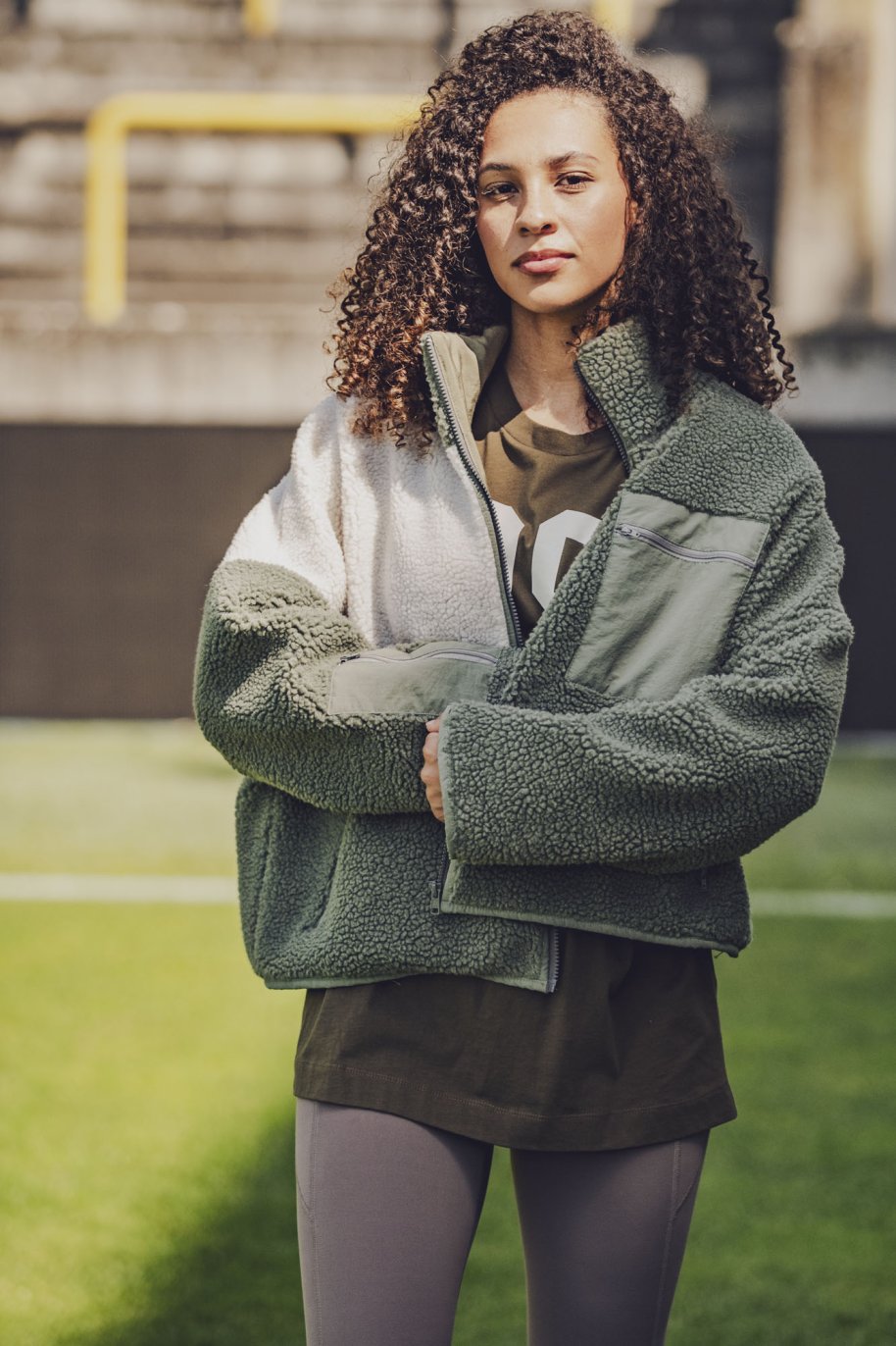 Woman wearing the Raya Jacket sewing pattern from Fibre Mood on The Fold Line. A lined jacket pattern made in teddy fabric, sherpa fleece, (faux) fur, bouclé, felt, leather, or chunky knit fabric, featuring a slightly oversized fit, stand-up collar, zip front, and zip pockets.