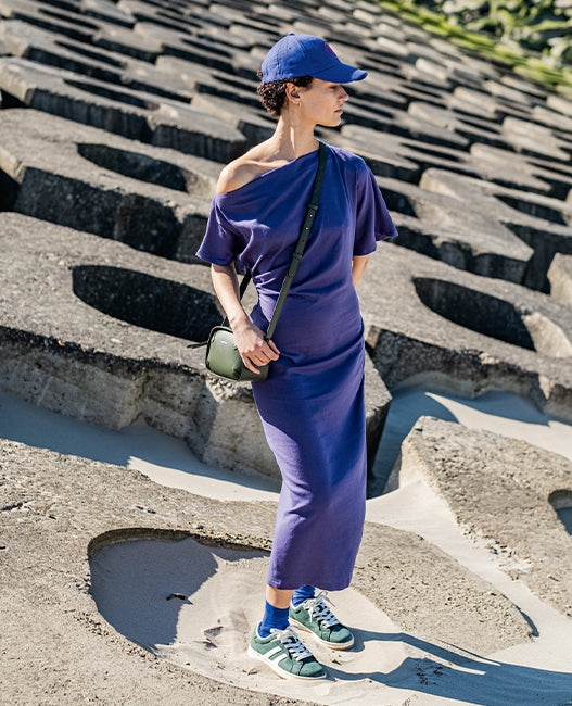 Woman wearing the Rebel Dress sewing pattern from Fibre Mood on The Fold Line. A dress pattern made in crepe, lyocell, cupro, satin, viscose, or knit fabric, featuring a tailored fit, asymmetrical shoulder line, short sleeves, drape at the waist, concealed side zip, and midi length.