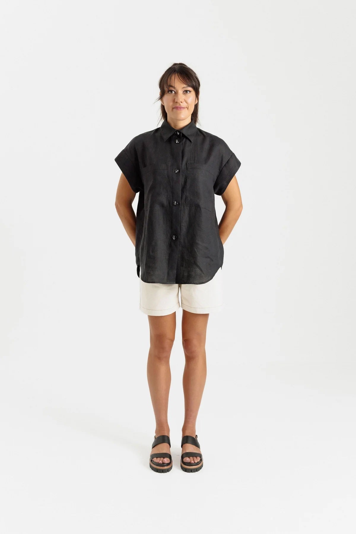 Woman wearing the Remy Shirt sewing pattern from Papercut Patterns on The Fold Line. A button front shirt pattern made in cotton, linen, denim, or flannel fabric, featuring drop shoulders with a cuff, a classic collar, patch pockets, and curved hem.