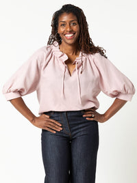 Woman wearing the Reynolds Woven Top sewing pattern from Style Arc on The Fold Line. A top pattern made in linen, rayon, or cotton fabric, featuring a relaxed fit, ruffle collar, slightly gathered neckline, split neck opening with rouleau ties, elbow length raglan sleeves gathered into cuffs, side splits, and hip length.