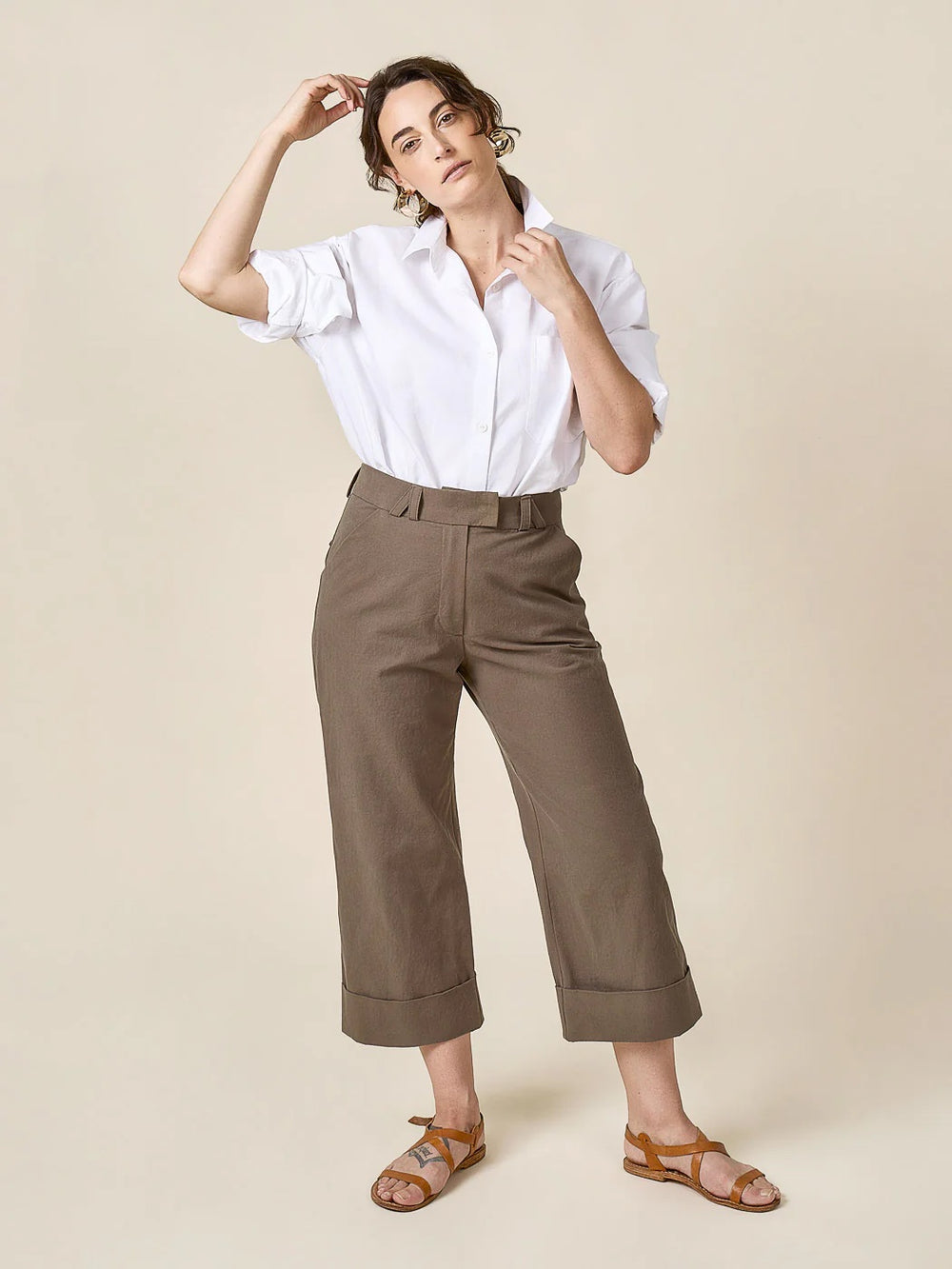 Woman wearing the Rika Pants sewing pattern from Closet Core Patterns on The Fold Line. A pants pattern made in cotton canvas, twill, denim, gabardine, or corduroy fabric, featuring a high rise sitting just below the natural waist, tabbed waistband with belt loops, fly front zipper, angled front pockets, rounded back pockets with flaps, and cropped straight legs with deep cuffs.