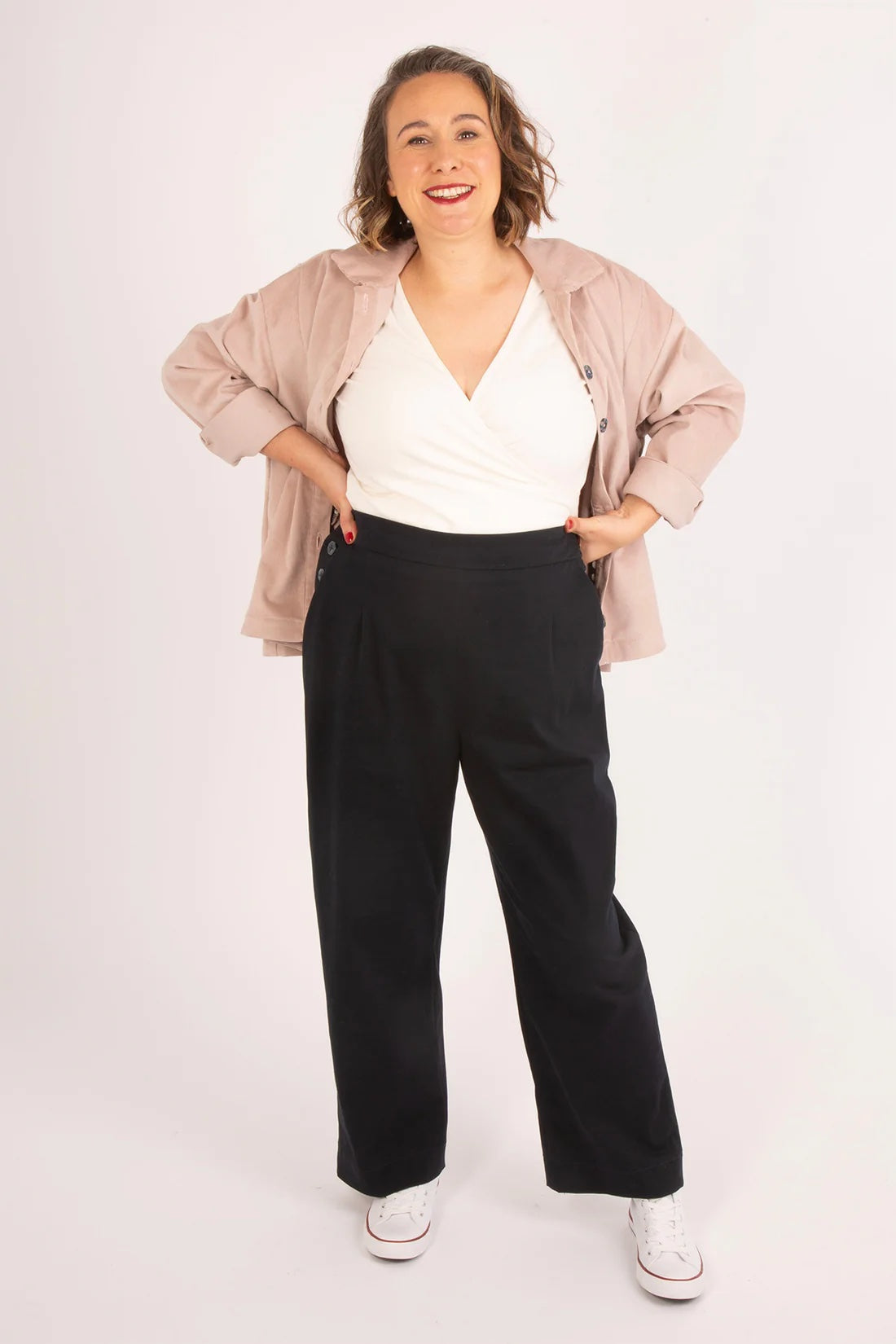Woman wearing the Rosemary Trousers sewing pattern from Sew Over It on The Fold Line. A trousers pattern made in cotton twill, stretch cotton, denim, or canvas fabric, featuring waist darts at the front and back, a flat front waistband and elasticated back waistband, side button opening, slanted pockets at the front, and patch pockets at the back.