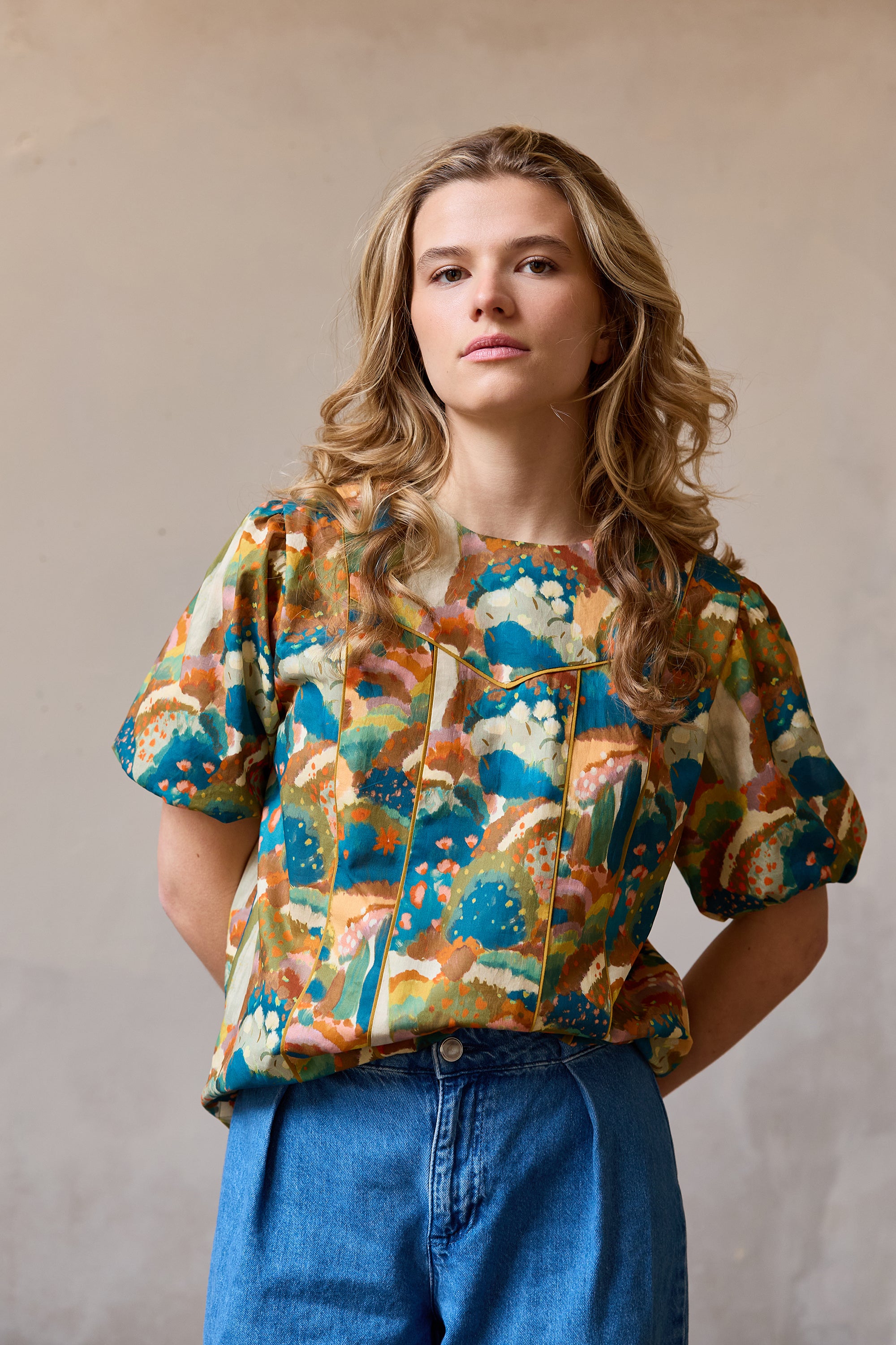 Woman wearing the Rosie Blouse sewing pattern from Atelier Jupe on The Fold Line. A top pattern made in viscose, cotton, tencel, linen, or polyester fabric, featuring a round neckline, panelled front, and short puffed sleeves.