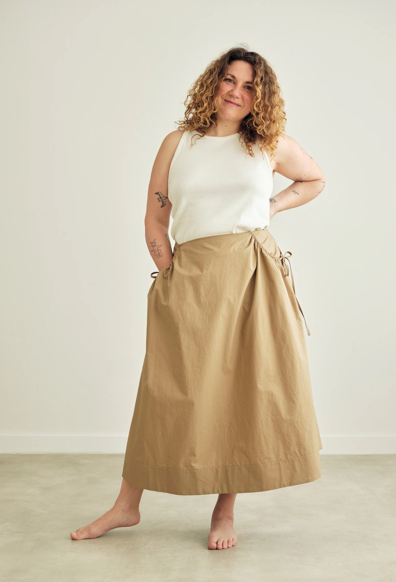 Woman wearing the Rowan Skirt sewing pattern from the Modern Sewing Co. on The Fold Line. A skirt pattern made in cotton lawn, poplin, seersucker, linen, cotton twill, lightweight wool or wool blends, or tencel fabric, featuring an A-line silhouette, gathered side pocket openings, deep hem facing, and midi length.