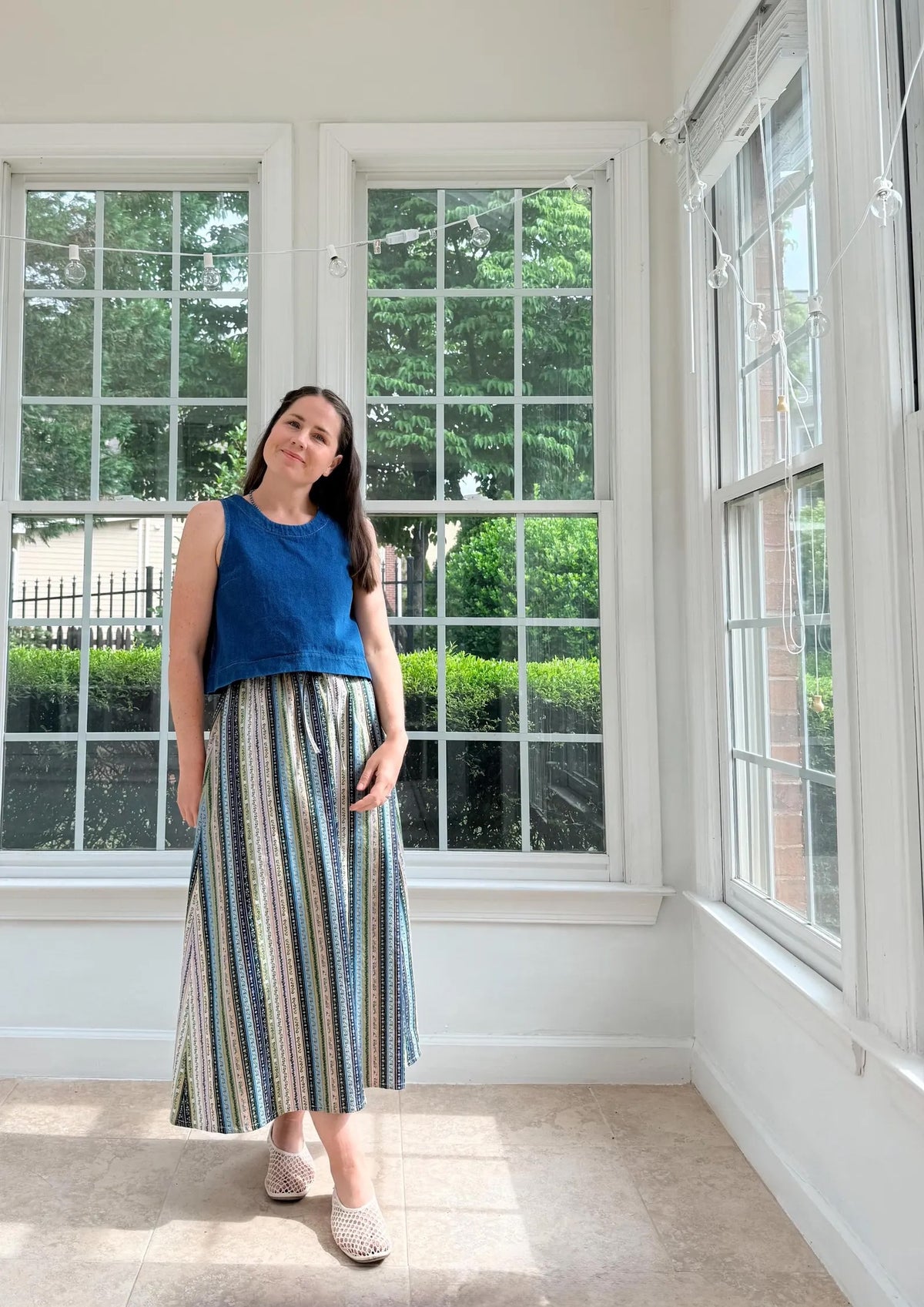 Woman wearing the Rowan Tank sewing pattern from Me & Kiddo Patterns on The Fold Line. A sleeveless top pattern made in cotton, linen, or denim fabric, featuring a relaxed fit, round neckline, bust darts, and slightly cropped length.