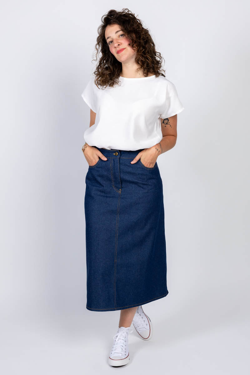 Woman wearing the Ruby Skirt sewing pattern from I AM Patterns on The Fold Line. A skirt pattern made in denim, gabardine, cotton twill, faux leather, suede, tencel twill, or corduroy fabric, featuring a fitted waistband, zip fly, front pockets, back pockets, back vent, and contrast topstitching. 