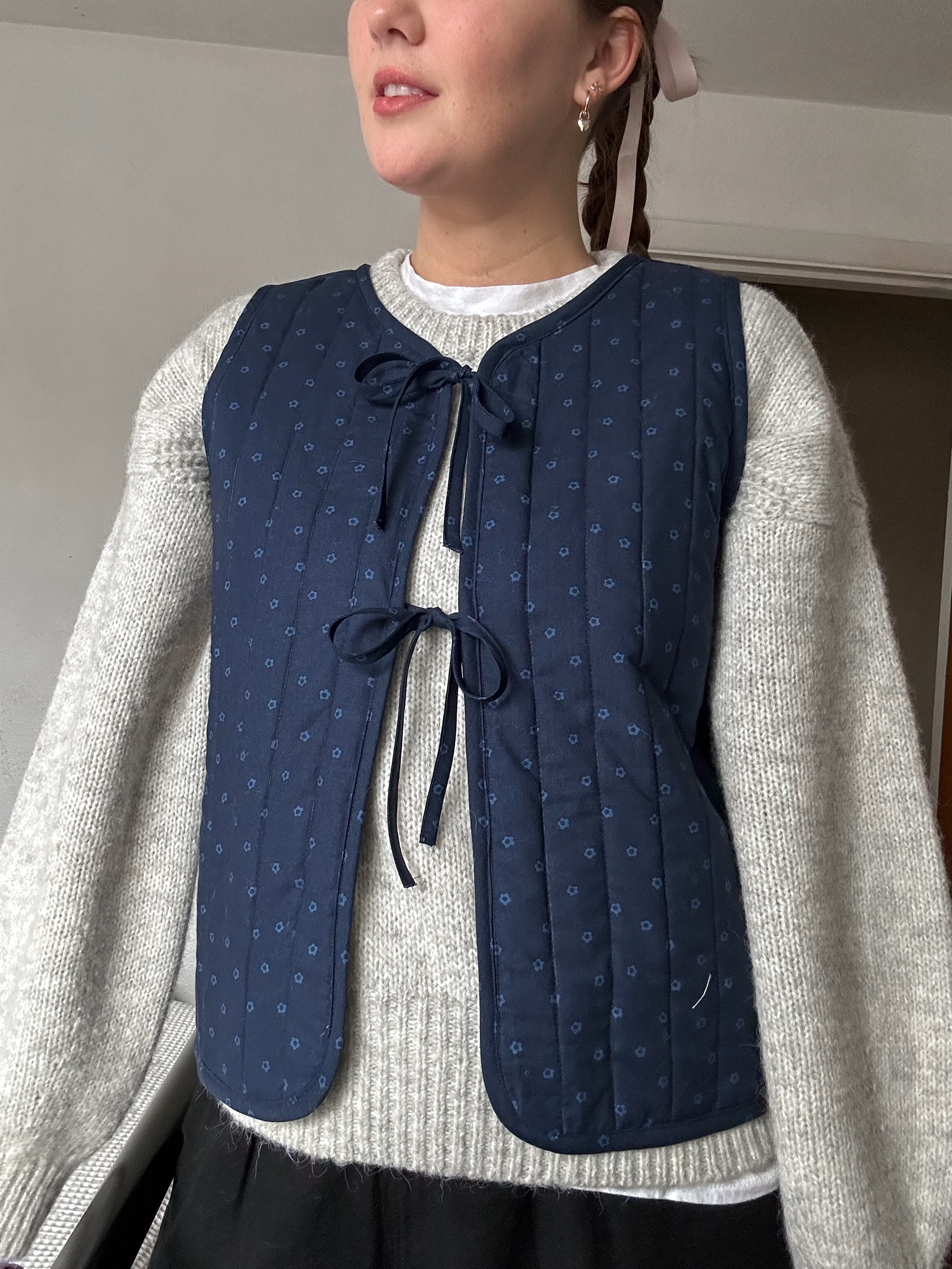 Woman wearing the Ruby Vest sewing pattern from Syd Graham Patterns on The Fold Line. A reversible waistcoat or gilet pattern made in cotton or linen fabric, featuring quilting, bias bound edges, and a tie front.