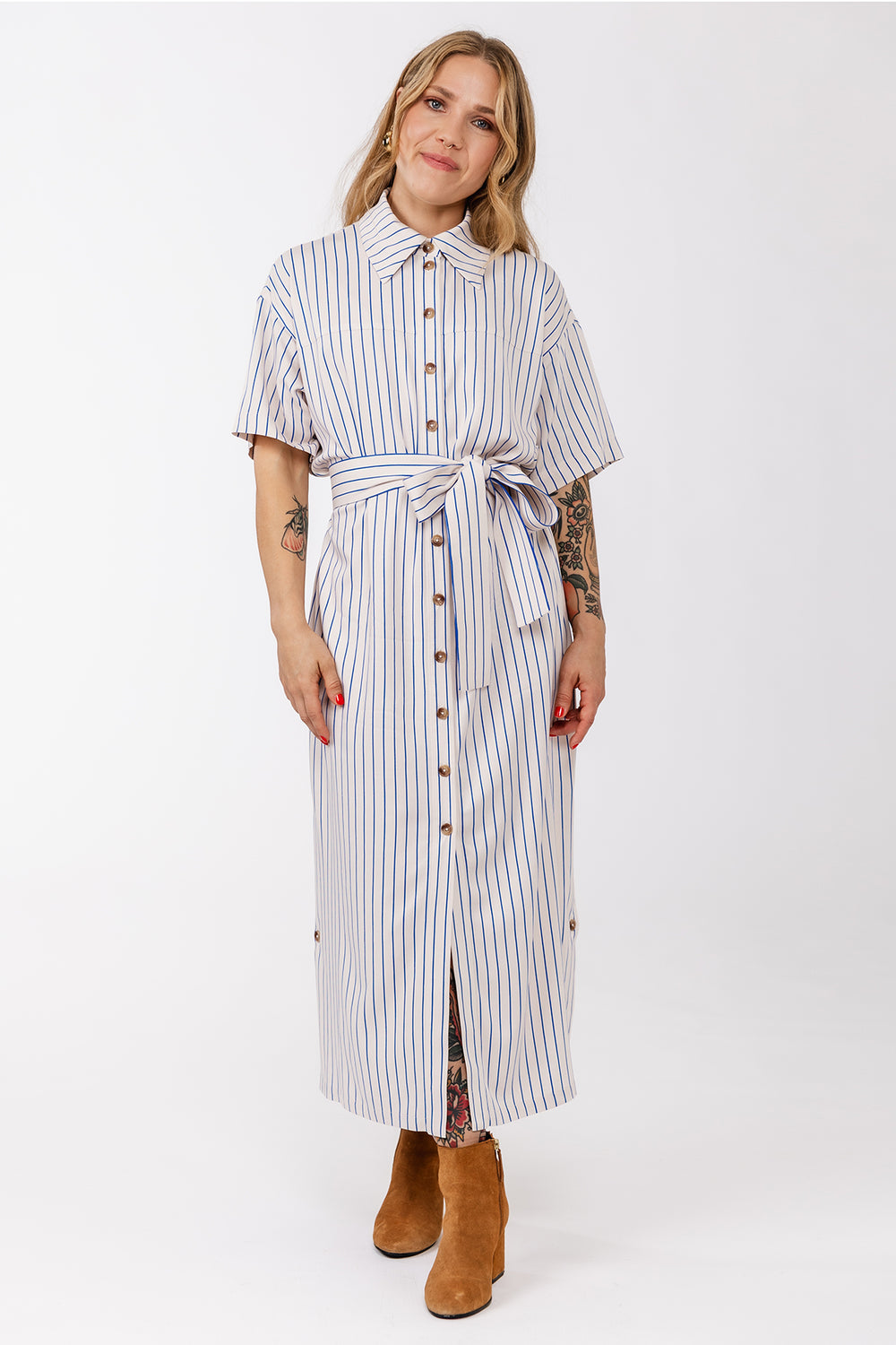 Woman wearing the Ruut Shirt Dress sewing pattern from Named on The Fold Line. A dress pattern made in voile, poplin, or light linen shirting fabric, featuring a relaxed fit, pointed collar, button front, short sleeves, tie belt, side pockets, buttoned vents at the hem, and midi length.