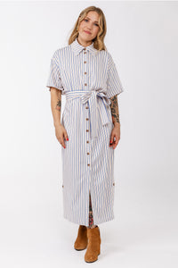 Woman wearing the Ruut Shirt Dress sewing pattern from Named on The Fold Line. A dress pattern made in voile, poplin, or light linen shirting fabric, featuring a relaxed fit, pointed collar, button front, short sleeves, tie belt, side pockets, buttoned vents at the hem, and midi length.