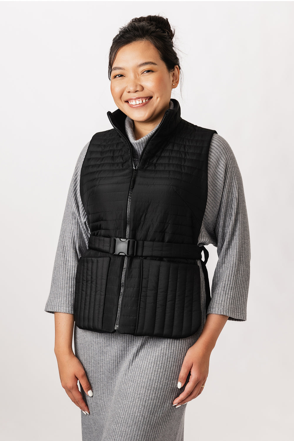 Woman wearing the Saana Puffer Vest sewing pattern from Named on The Fold Line. A lined puffer vest pattern made in quilted fabric, featuring a high collar, zip fastening, patch pockets, open sides, and a belt with a clip buckle. 