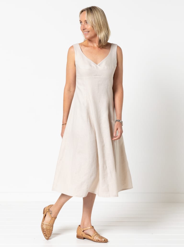 Woman wearing the Sabrina Woven Dress sewing pattern from Style Arc on The Fold Line. A sleeveless dress pattern made in linen, crepe, or stretch sateen fabric, featuring a fit-and-flare silhouette, low neckline, high waisted bodice, gored skirt, and below knee length.