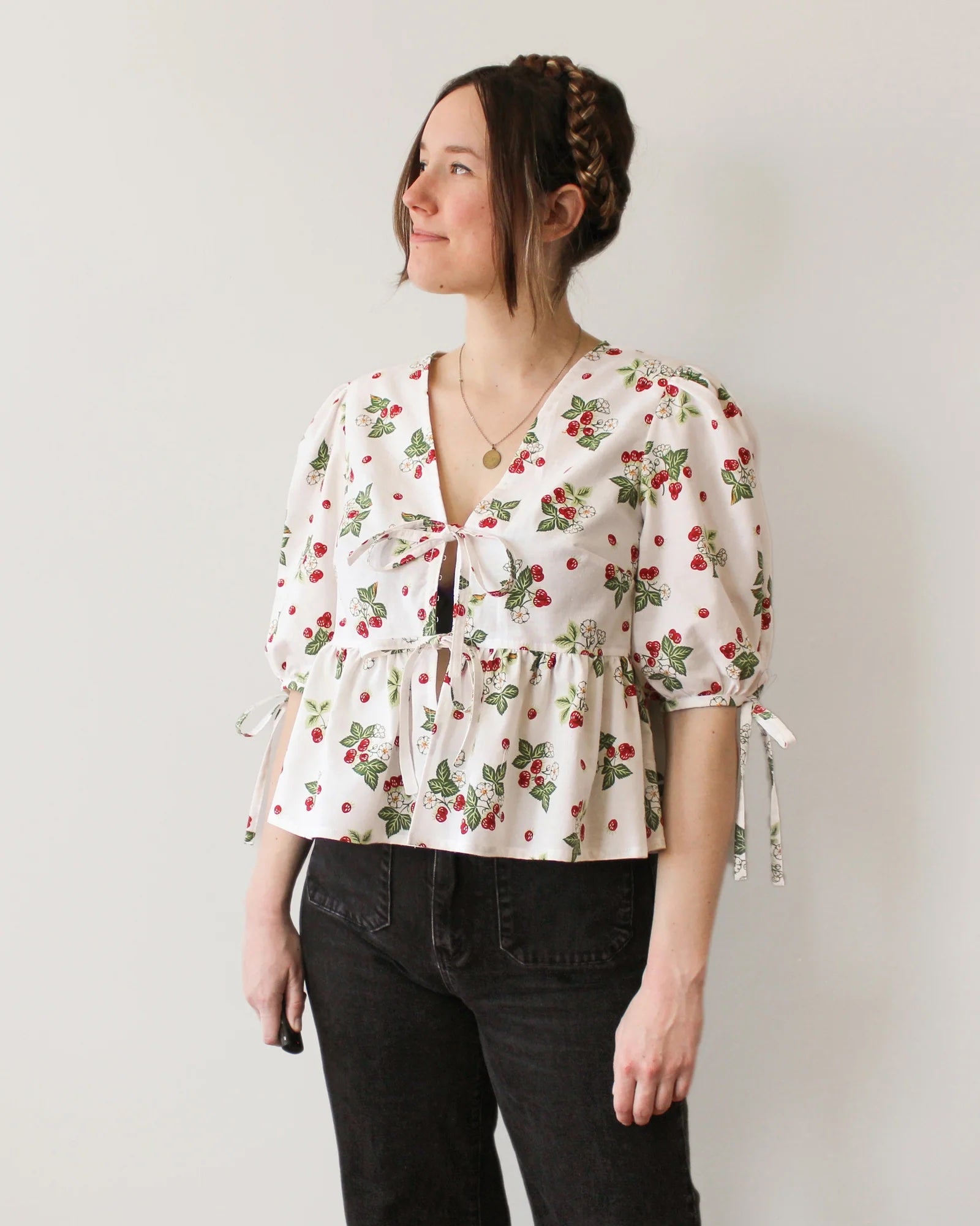 Woman wearing the Sadie Top sewing pattern from Oh Me Oh My Sewing on The Fold Line. A blouse pattern made in quilting cotton, washed linen, viscose, cotton lawn, voile, or rayon challis fabric, featuring a relaxed fit, V-shaped neckline, tie front closure, elbow length sleeves with ties, and gathered peplum.
