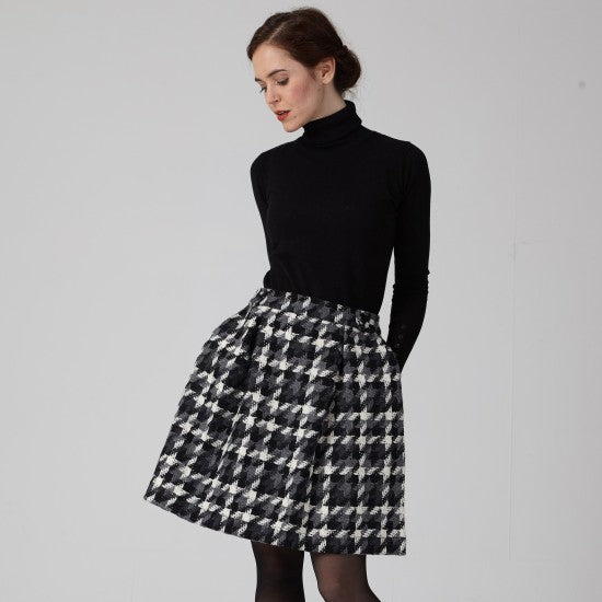 Woman wearing the Salomé Skirt sewing pattern from Coralie Bijasson on The Fold Line. A skirt pattern made in neoprene, cotton, jacquard, or wool fabric, featuring box pleats, pockets with hidden gussets, a waistband with snaps, and mini length.