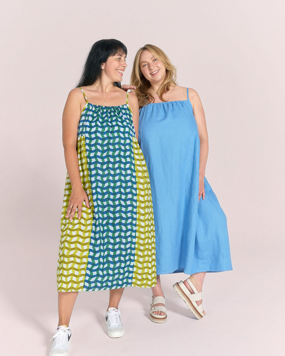 Women wearing the Schoolhouse Sundress sewing pattern from Matchy Matchy Sewing Club on The Fold Line. A dress pattern made in lightweight cotton or linen fabric, featuring a relaxed silhouette, spaghetti straps, softly gathered neckline, high waist with gathered side panels, and midi length.