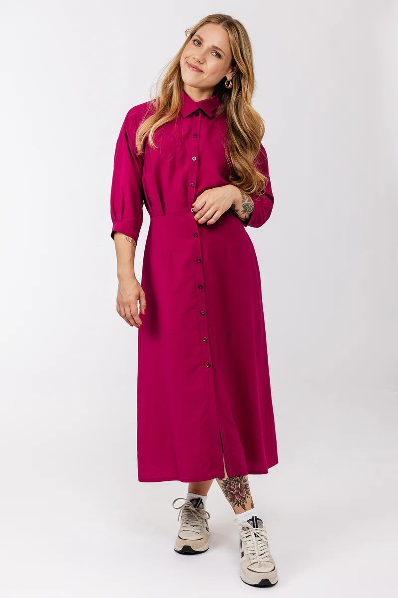 Woman wearing the Silmu Shirt Dress sewing pattern from Named on The Fold Line. A dress pattern made in shirting fabric, featuring an overlapping collar, button front, waist pleats, pleated half sleeves, a tie closure at the back, and midi length.