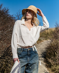 Woman wearing the Siren Blouse sewing pattern from Fibre Mood on The Fold Line. A shirt pattern made in poplin, cotton, seersucker, nylon, organza, viscose satin, double gauze, chambray, lyocell, or crepe fabric, featuring a relaxed fit, collar, wrap front, long sleeves with cuffs, chest pockets, and a gathered hem.