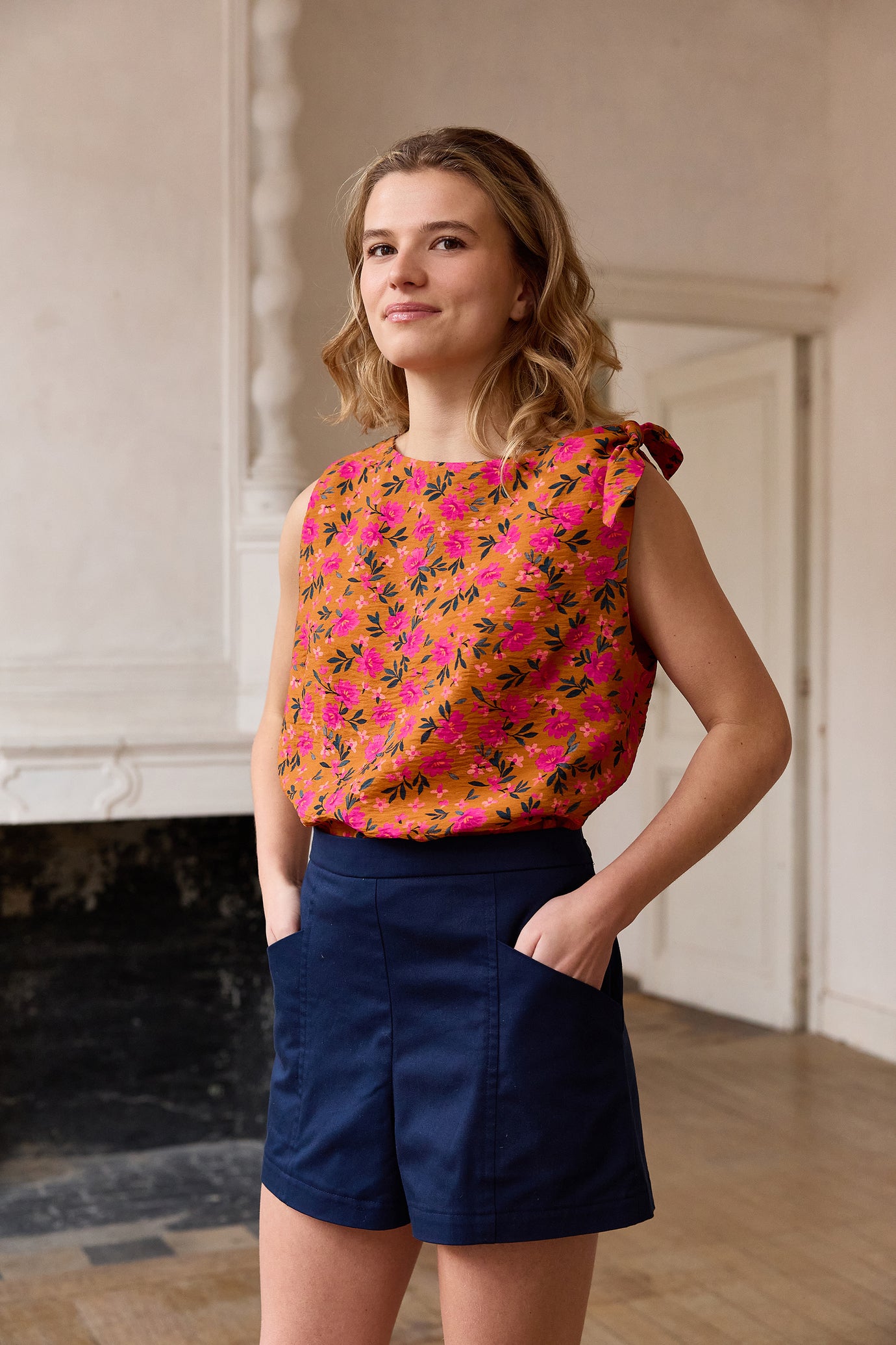 Woman wearing the Sophie Top and Ellis Shorts sewing pattern from Atelier Jupe on The Fold Line. A sleeveless top and shorts pattern made in viscose, cotton, tencel, linen, double gauze, polyester, denim, gabardine, or jacquard fabric, featuring a boat neckline and knot at the left shoulder for the top and a waistband, invisible zipper, and pockets for the shorts.