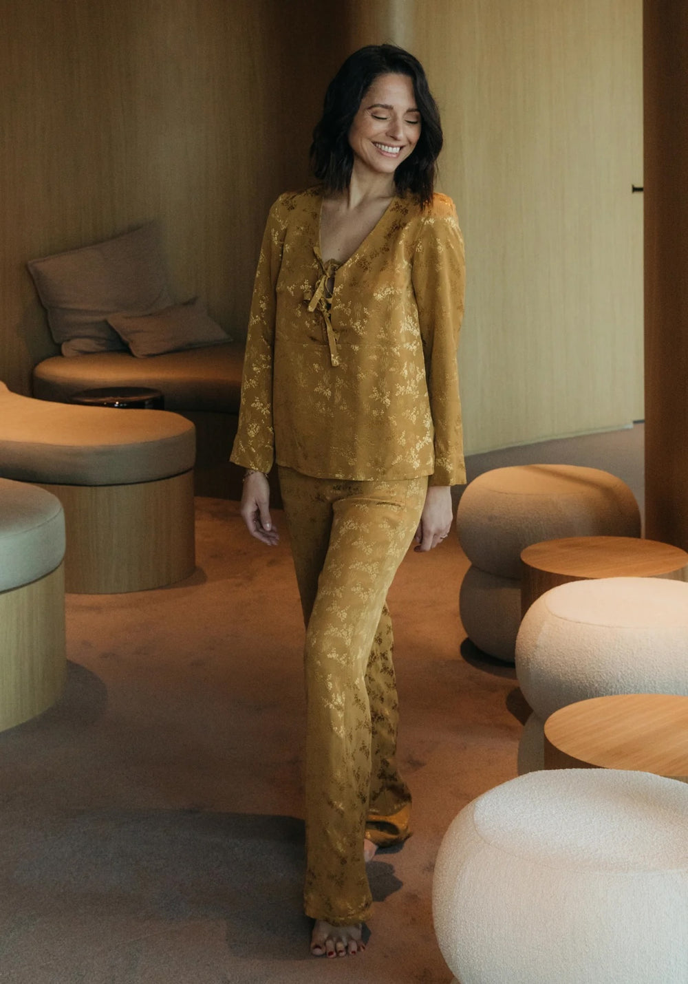 Woman wearing the Soupir Pyjamas sewing pattern from Maison Fauve on The Fold Line. A pyjamas pattern made in cotton, viscose, cupro, or tencel fabric, featuring a top with a scoop neckline, front ties, and long sleeves, and pants with a straight cut, elasticated back waist, and pockets.