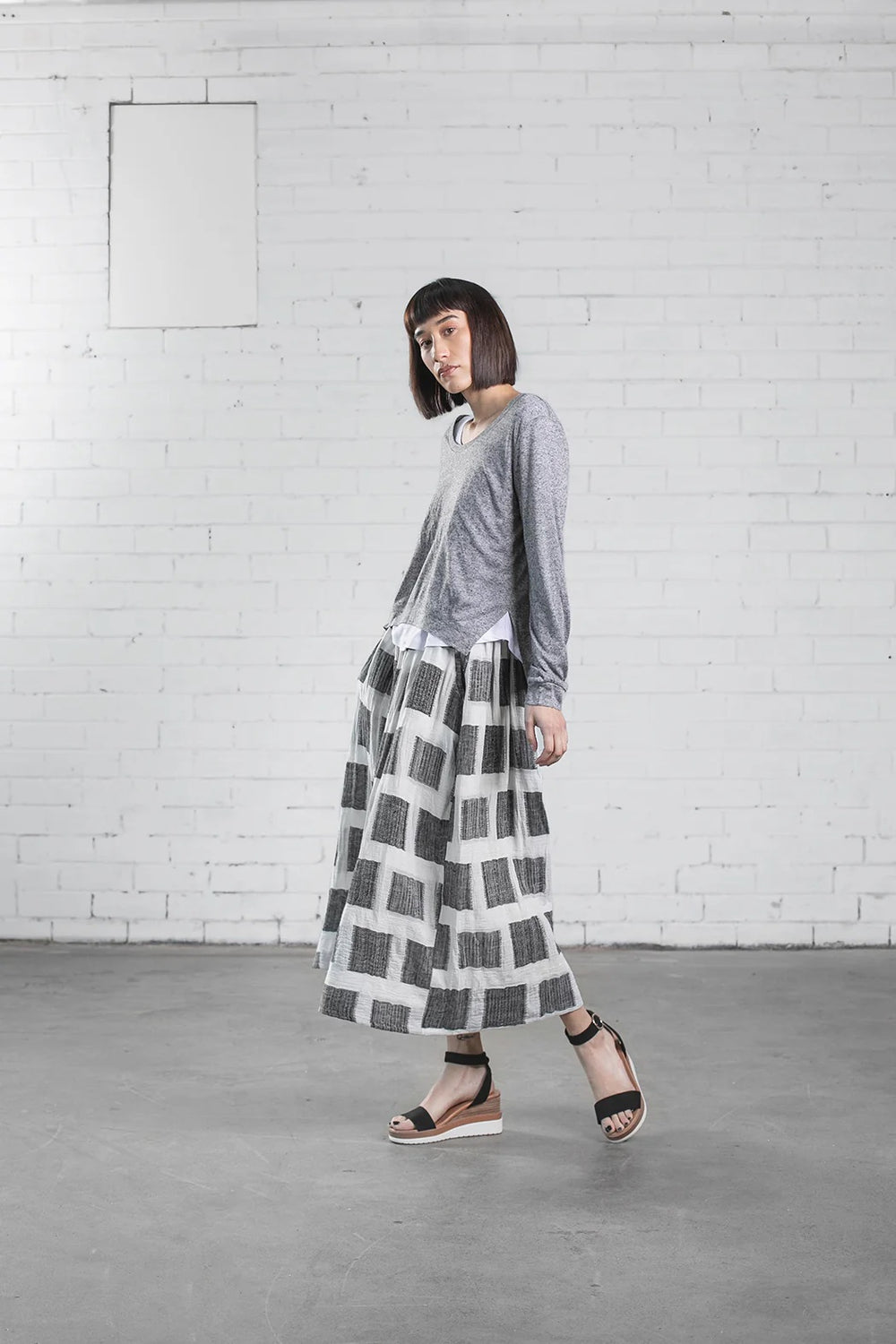 Woman wearing the Staley Top sewing pattern from Elbe Textiles on The Fold Line. A top pattern made in knit fabric, featuring a long sleeve top with a scooped neckline and split hem layered over a short sleeve T-shirt with a scooped neckline and curved hem.