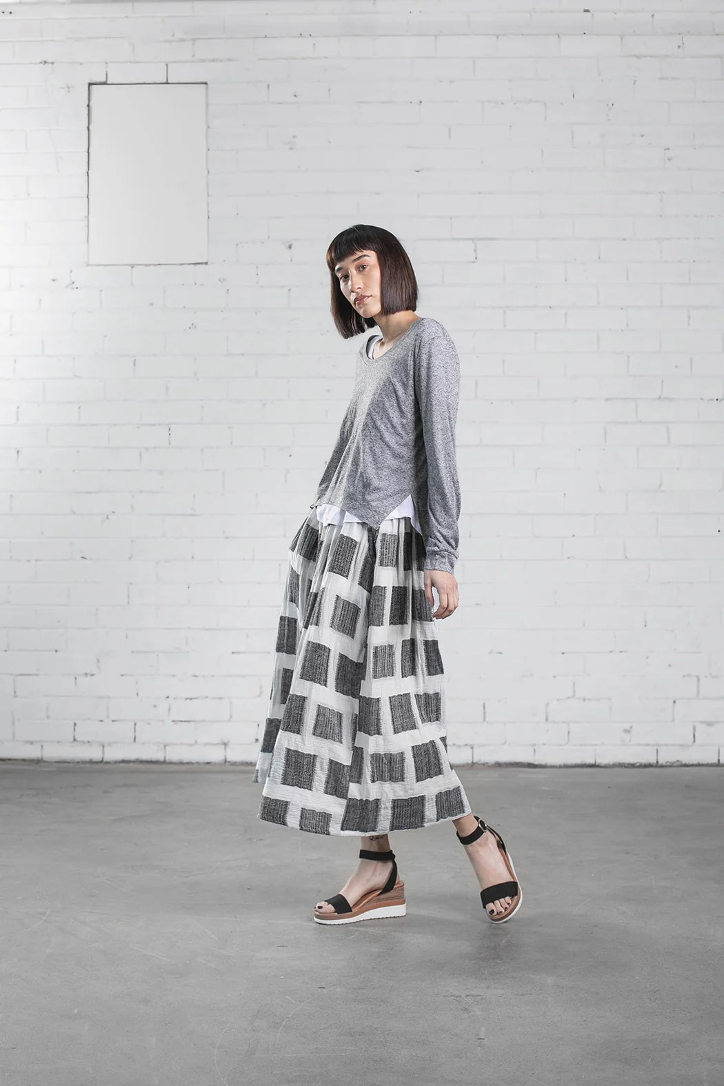 Woman wearing the Staley Top sewing pattern from Elbe Textiles on The Fold Line. A top pattern made in knit fabric, featuring a long sleeve top with a scooped neckline and split hem layered over a short sleeve T-shirt with a scooped neckline and curved hem.