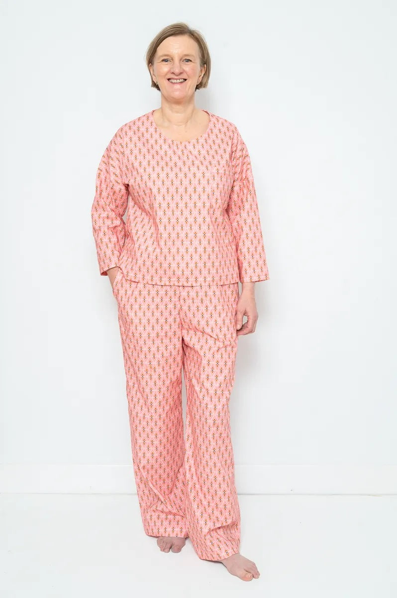 Woman wearing the Susy Pyjamas sewing pattern from Bobbins and Buttons on The Fold Line. A pyjamas pattern made in cotton fabric, featuring a top with a round neck and long sleeves, and full length trousers with an elasticated waist and in-seam pockets.