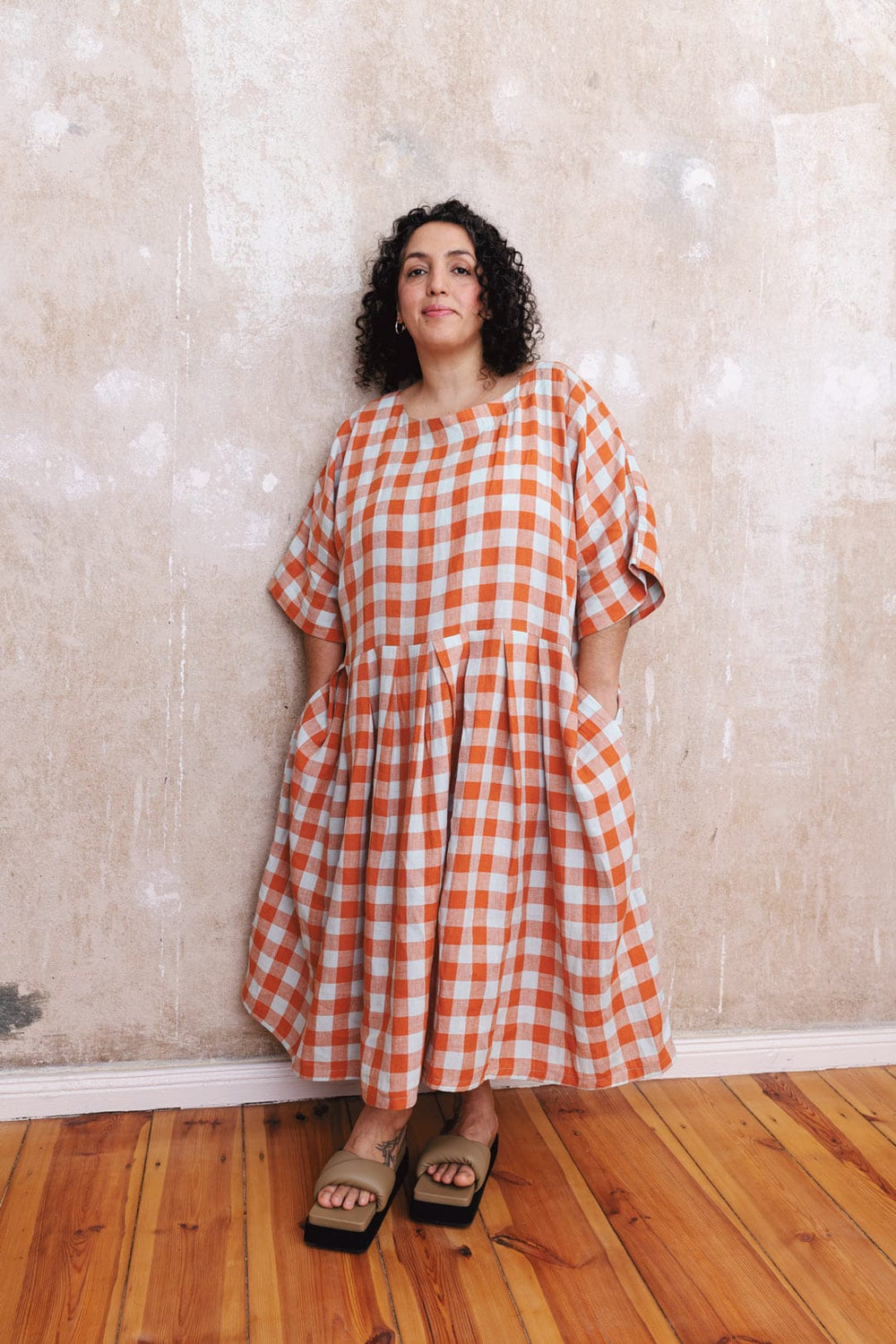 Woman wearing the Swing Dress sewing pattern from TAUKO on The Fold Line. A dress pattern made in linen, cotton, or denim fabric, featuring a relaxed fit, round neckline, grown-on sleeves, pleated skirt, and side pockets.