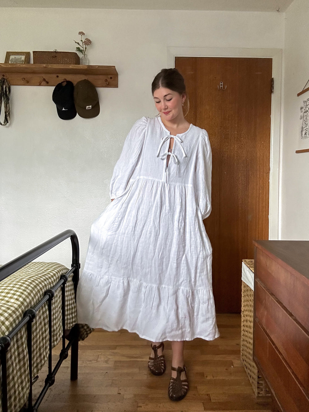 Woman wearing the Syd Tie Dress sewing pattern from Syd Graham Patterns on The Fold Line. A dress pattern made in cotton or linen fabric, featuring a round neckline, tie front closure, 3/4 length puffy sleeves, gathered tiers, and midi length.