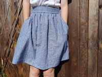 Girl wearing the Teens' Eucalyptus Skirt sewing pattern from Waves & Wild on The Fold Line. A skirt pattern made in cotton poplin or linen fabric, featuring an elasticated waist with a flat front, pockets, and knee length.