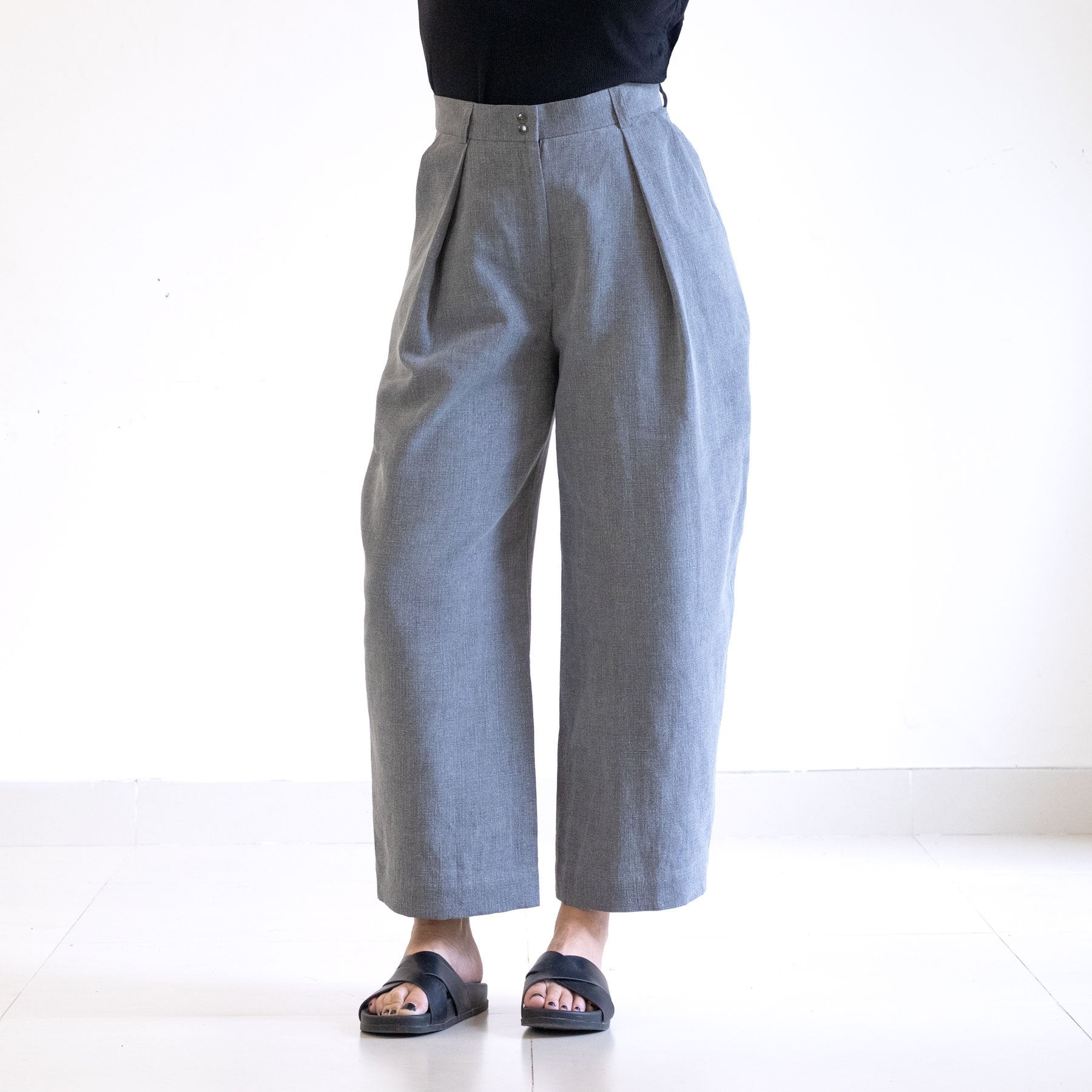 Woman wearing the Terra Pants sewing pattern from Pattern Fantastique on The Fold Line. A trousers pattern made in cotton, denim, linen, corduroy, or velvet fabric, featuring a high waist, zip fly, deep pleats, pockets, belt loops, and tapered and slightly bowed leg.