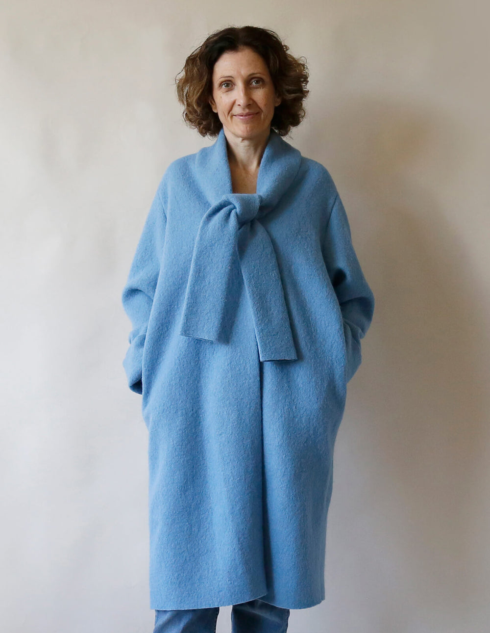 Woman wearing the Tie Front Cardigan Coat sewing pattern from The Maker's Atelier on The Fold Line. A coatigan pattern made in washed or boiled wool fabric, featuring a scarf tie, long sleeves, and in-seam pockets.