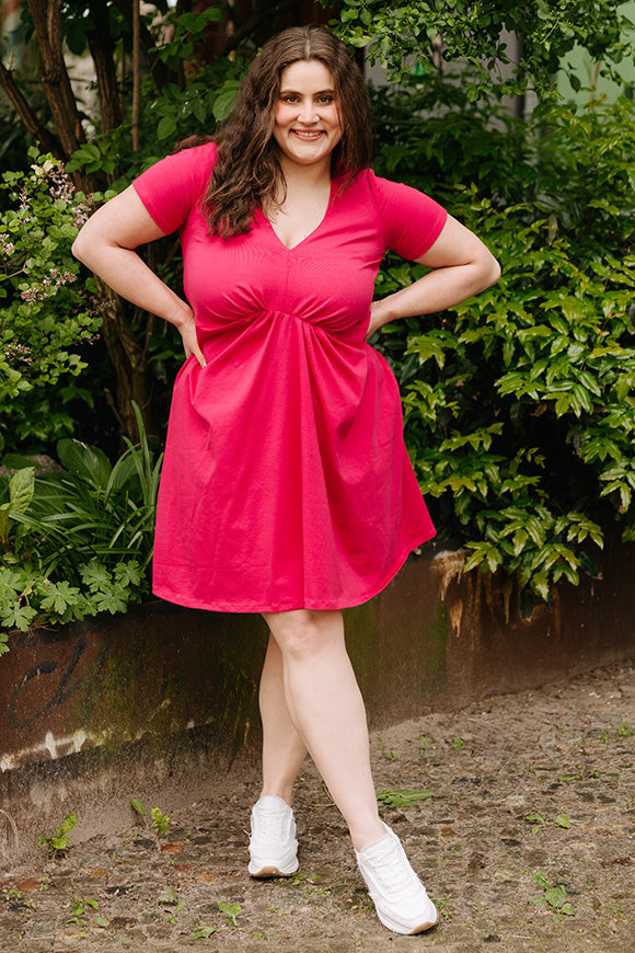 Woman wearing the Tilly Dress sewing pattern from JULIANA MARTEJEVS on The Fold Line. A dress pattern made in knit fabric, featuring a deep V-neckline, short sleeves, gathered front, and mini length.