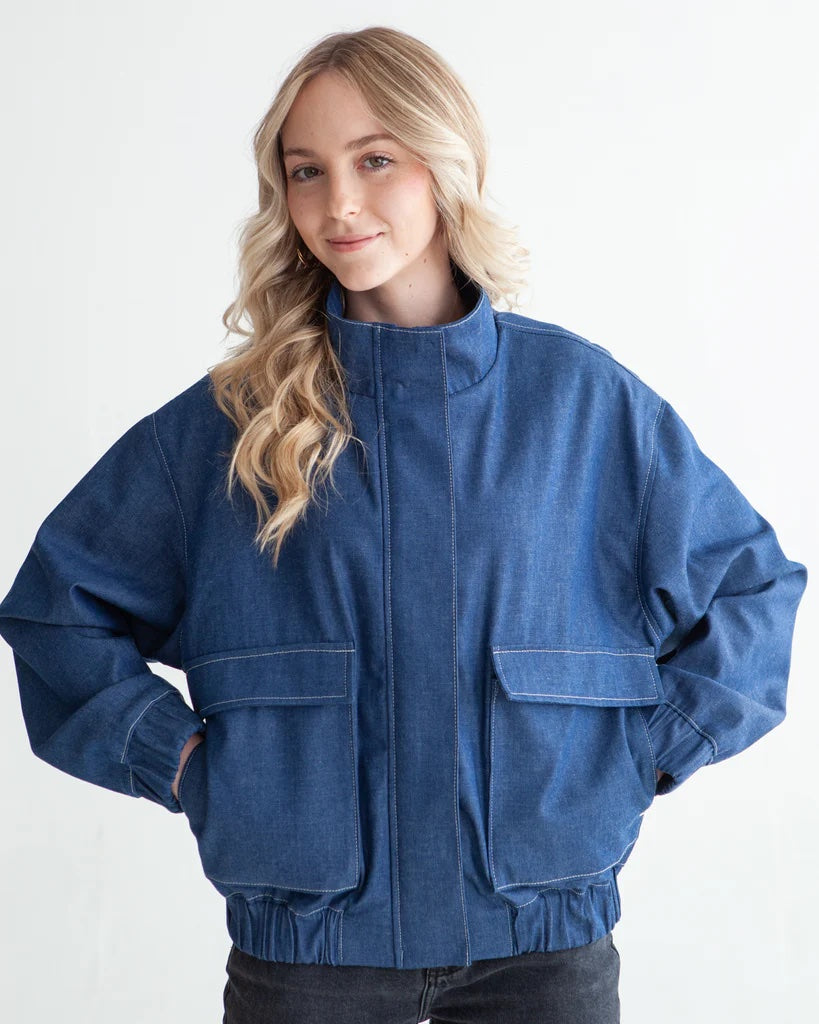 Woman wearing the Tobie Jacket sewing pattern from True Bias on The Fold Line. A bomber jacket pattern made in cotton, corduroy, twill, denim, wool, suiting, or linen fabric, featuring an oversized fit, full lining, dropped shoulders, funnel collar, centre front zipper with cover, and patch pockets with flaps.