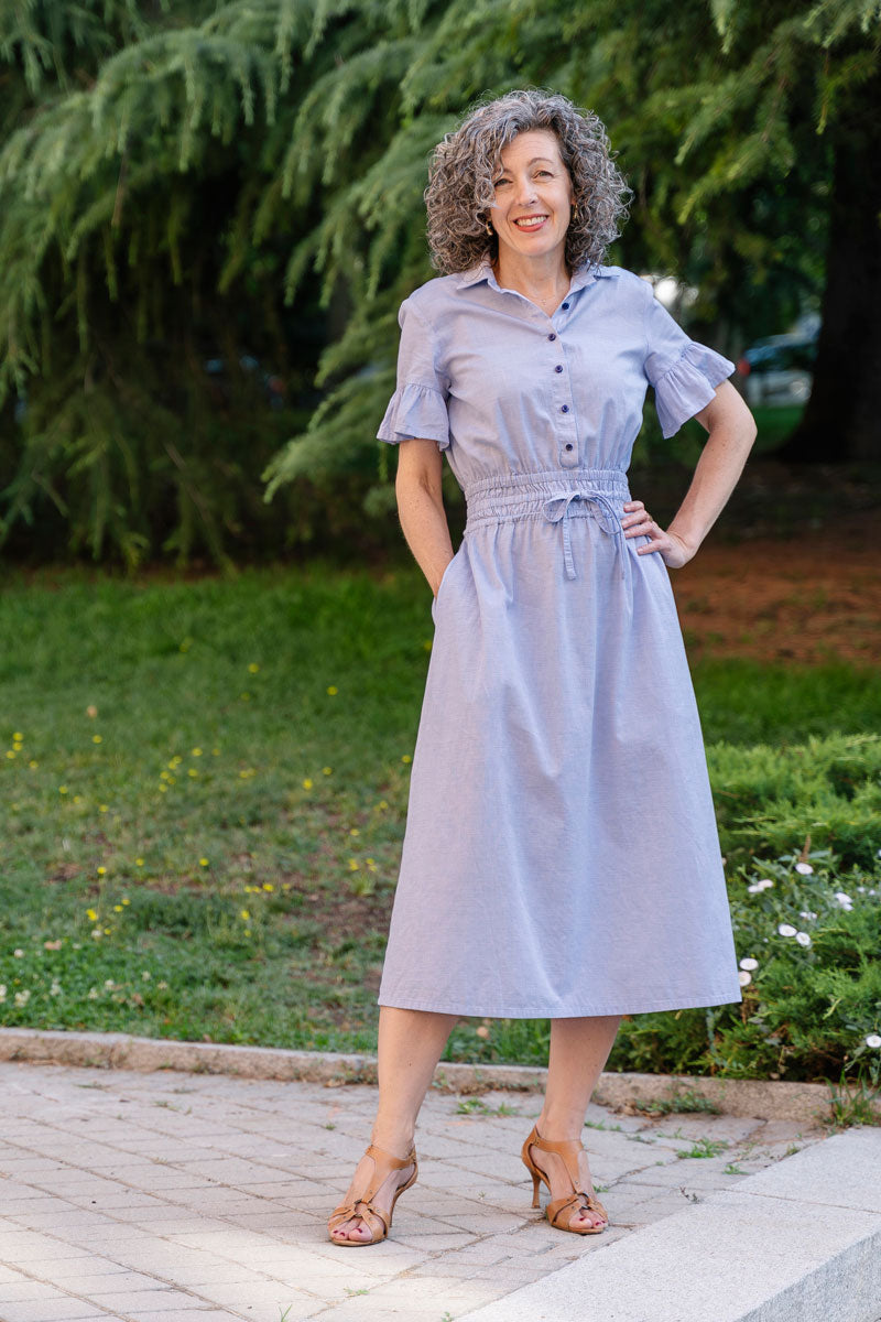 Woman wearing the Tomigaya Shirt Dress sewing pattern from Liesl + Co on The Fold Line. A shirt dress pattern made in cotton voile, lawn, shirting, linen, lightweight crepe, or rayon fabric, featuring a classic collar, button front, elastic waist with a drawstring, short sleeves with a ruffle, pockets, and a below-the-knee skirt.