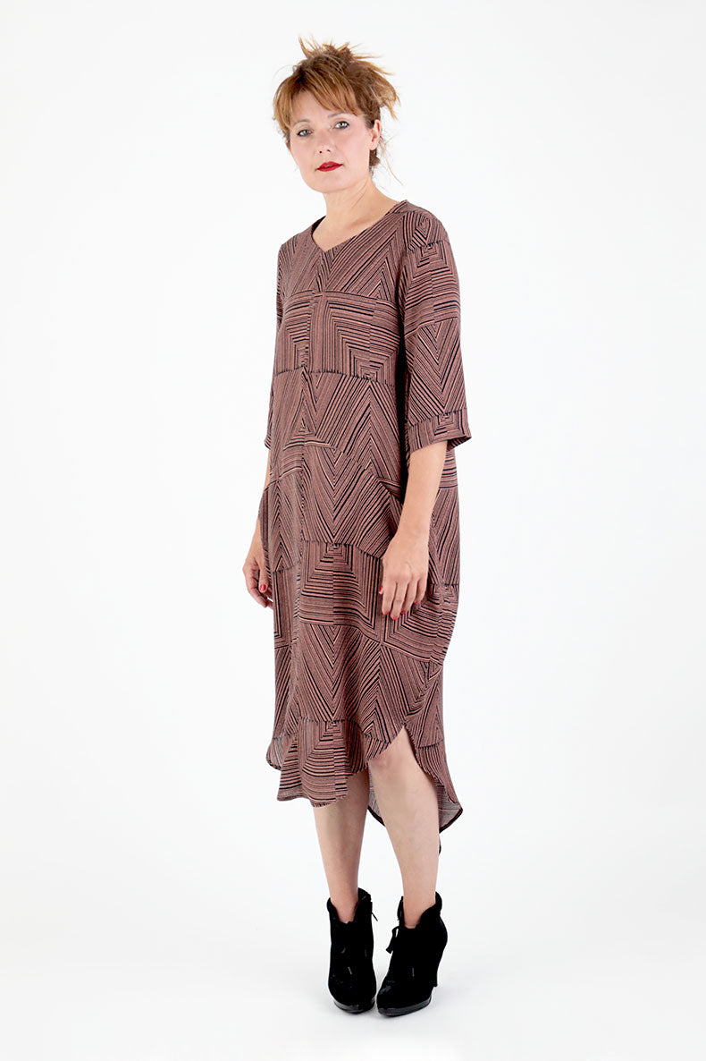 Woman wearing the Trine Cocoon Dress sewing pattern from Schnittchen Patterns on The Fold Line. A dress pattern made in crepe, viscose, light cotton, or linen fabric, featuring front pockets inserted into diagonal seamlines, elbow length sleeves, a rounded high-low hemline, and below the knee length.