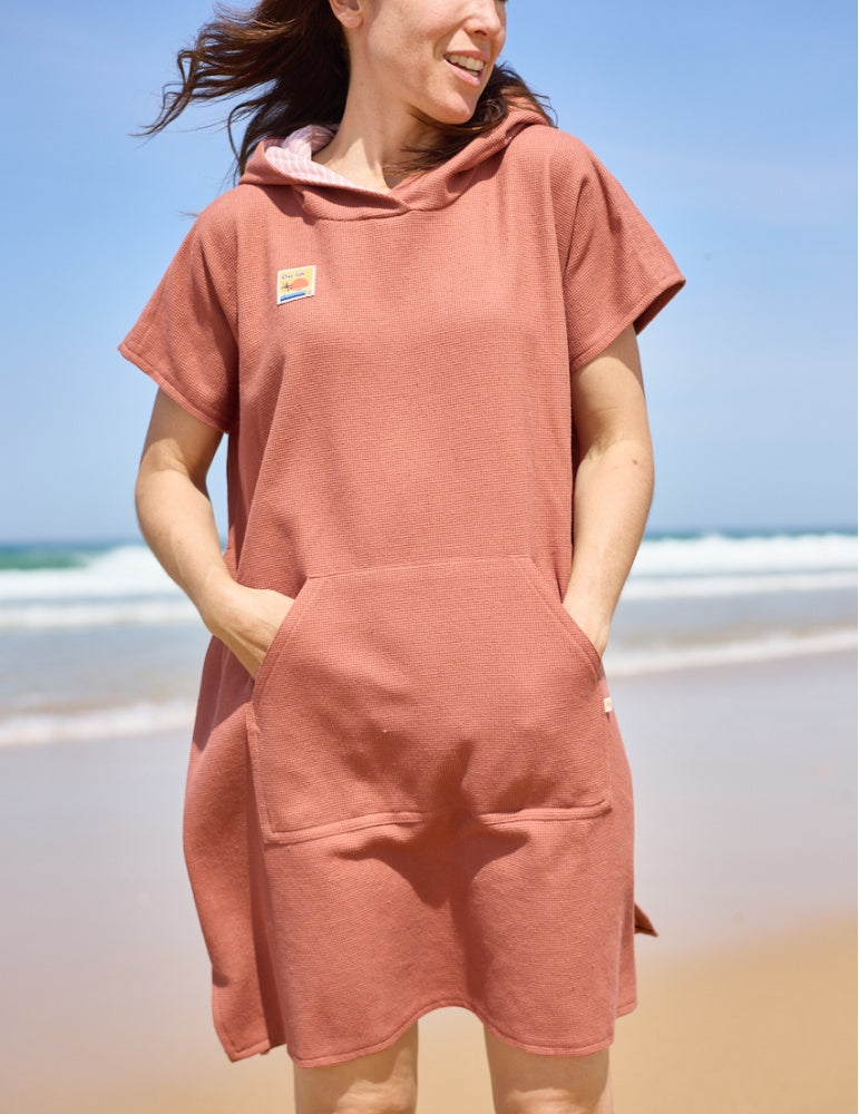 Woman wearing the Tropique Poncho sewing pattern from Atelier Scämmit on The Fold Line. A beach cover up pattern made in cotton, bamboo, terrycloth, microfibre, or waffle weave fabric, featuring a hood, kangaroo pocket, and side opening for easy changing.