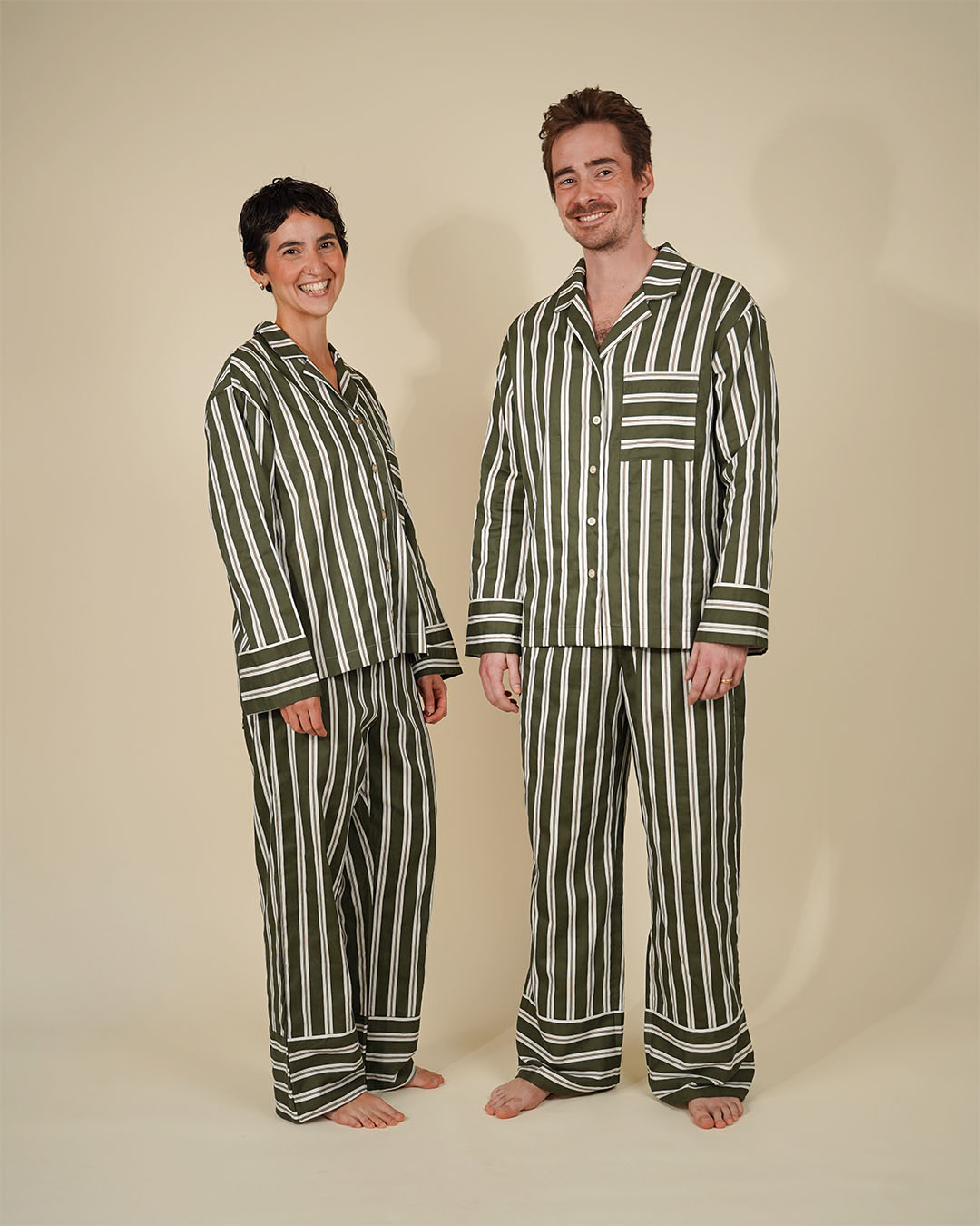 Man and woman wearing the Unisex Pyjama Set sewing pattern from Wardrobe by Me on The Fold Line. A pyjamas pattern made in cotton fabric, featuring a relaxed fit shirt with a convertible collar, dropped shoulders, long sleeves, button front, and chest pocket, and pants with an elastic waist and back pocket.
