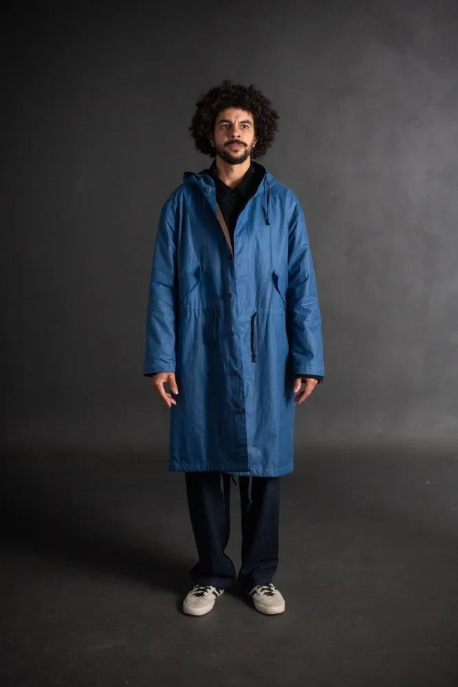 Man wearing the Unisex TN34 Parka sewing pattern from Merchant & Mills on The Fold Line. A coat pattern made in dry oilskin, oilskin, tweed, woollens, cotton drill, cotton canvas, waterproofed cotton or linen fabric, featuring a lining, hood, pockets, and fishtail hem.