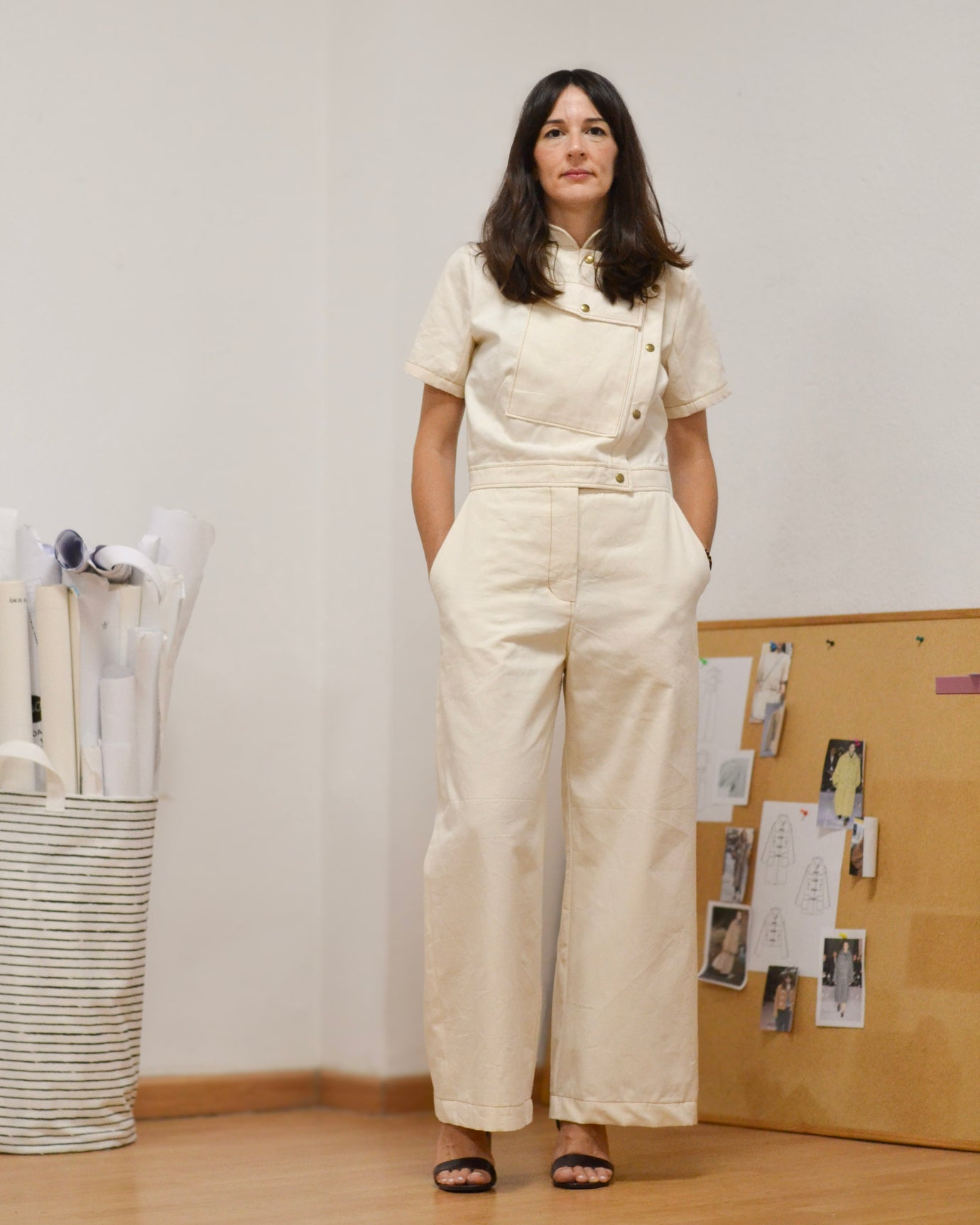 Woman wearing the Veles Boilersuit sewing pattern from Pauline Alice on The Fold Line. A jumpsuit pattern made in poplin, twill, denim, linen, flannel, or corduroy fabric, featuring a stand-up collar, asymmetrical buttoned opening, large flap pocket, short sleeves, adjustable waistband, fly front, wide legs, front slant pockets, and back patch pockets.