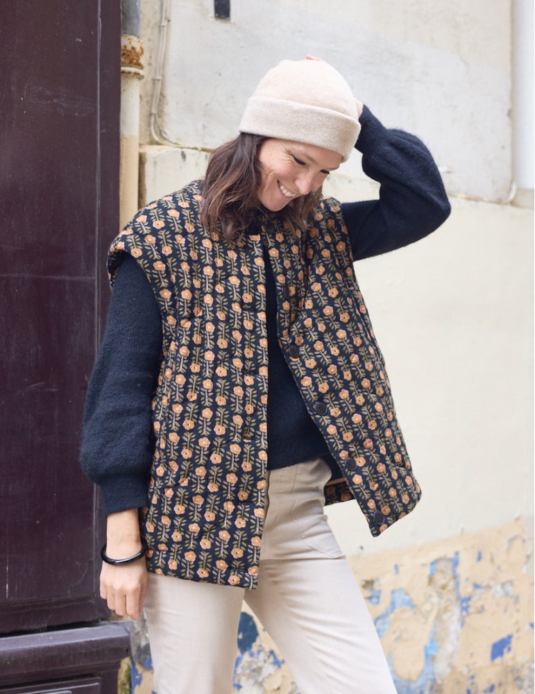 Woman wearing the Viva Jacket sewing pattern from Atelier Scämmit on The Fold Line. A sleeveless jacket pattern made in woollen, jacquard, quilted, or sherpa fabric, featuring a round neckline, dropped shoulder, button front, and welt pockets.