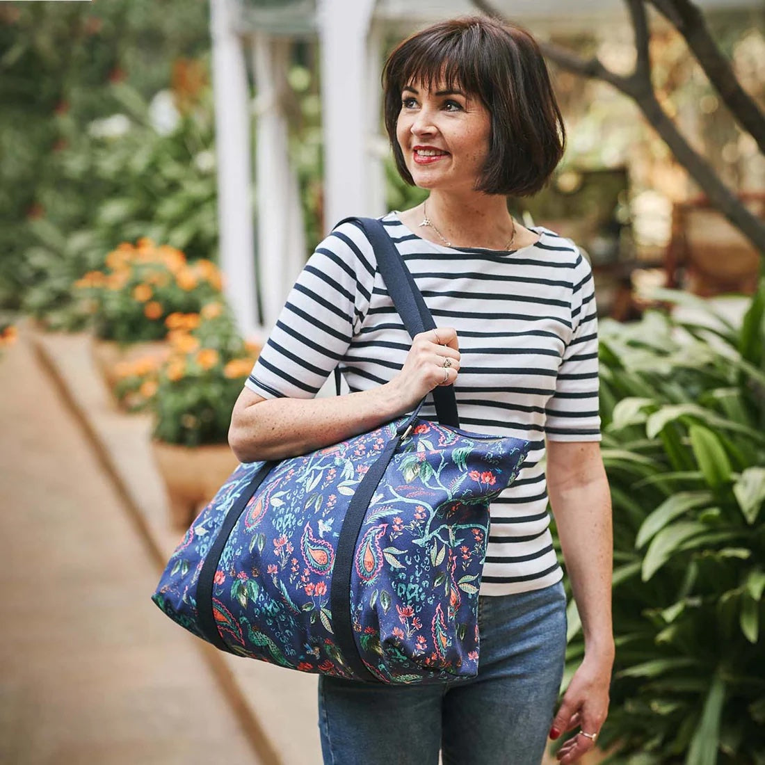 Woman carrying the Weekend Bag sewing pattern from Sew Over It on The Fold Line. A bag pattern made in cotton or canvas fabric, featuring a roomy interior, zip top, outer pocket, and webbing handles.
