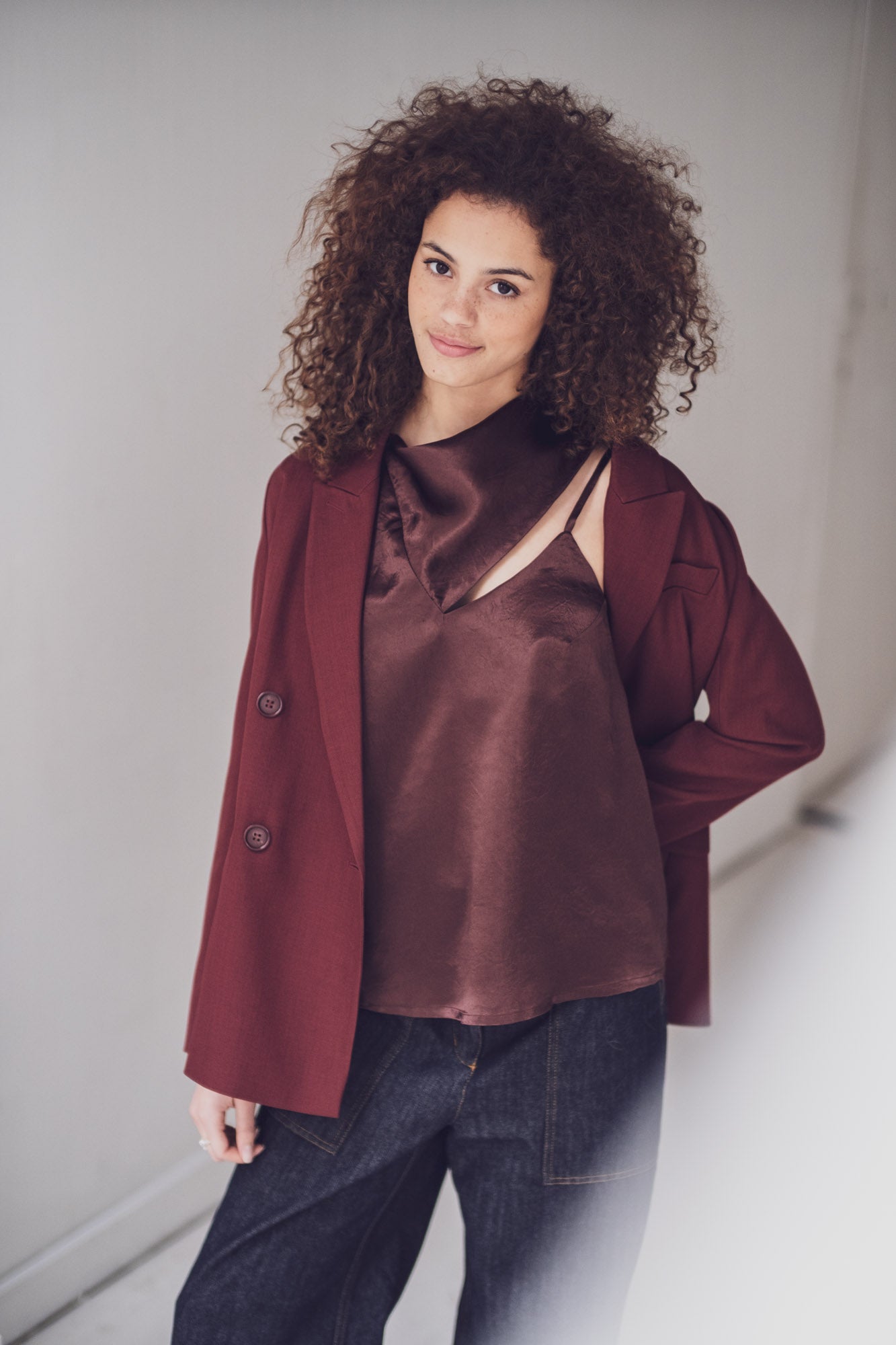 Woman wearing the Willow Top sewing pattern from Fibre Mood on The Fold Line. A sleeveless top pattern made in lyocell twill, satin, acetate, poplin, or chambray fabric, featuring an asymmetrical cut, one wide shoulder strap, one spaghetti strap, deep back neckline, and integrated scarf.