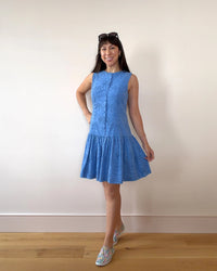 Woman wearing the Wimbledon Drop-Waist Dress sewing pattern from Nina Lee on The Fold Line. A sleeveless dress pattern made in cotton lawn, cotton poplin, crepe, chambray, lightweight wool, or lightweight needlecord fabric, featuring a fitted bodice with a faux button front, invisible zipper at the back, and short gathered skirt.