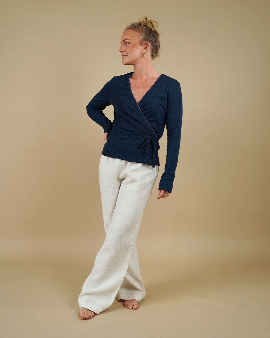 Woman wearing the Wrap Blouse sewing pattern from Wardrobe by Me on The Fold Line. A top pattern made in lightweight jersey fabric, featuring a wrap front that ties at the waist, a deep V-neckline, and long sleeves. 